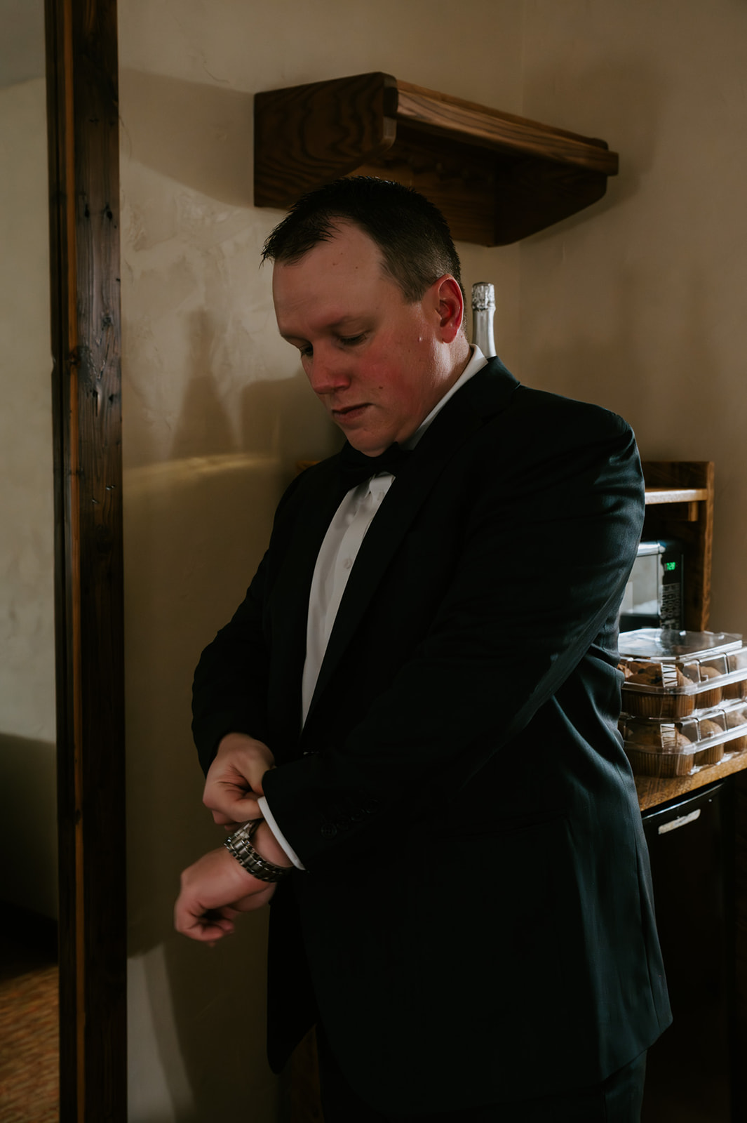 Groom buttoning his suit jacket in a warmly lit hotel room before heading out for their elopement video.