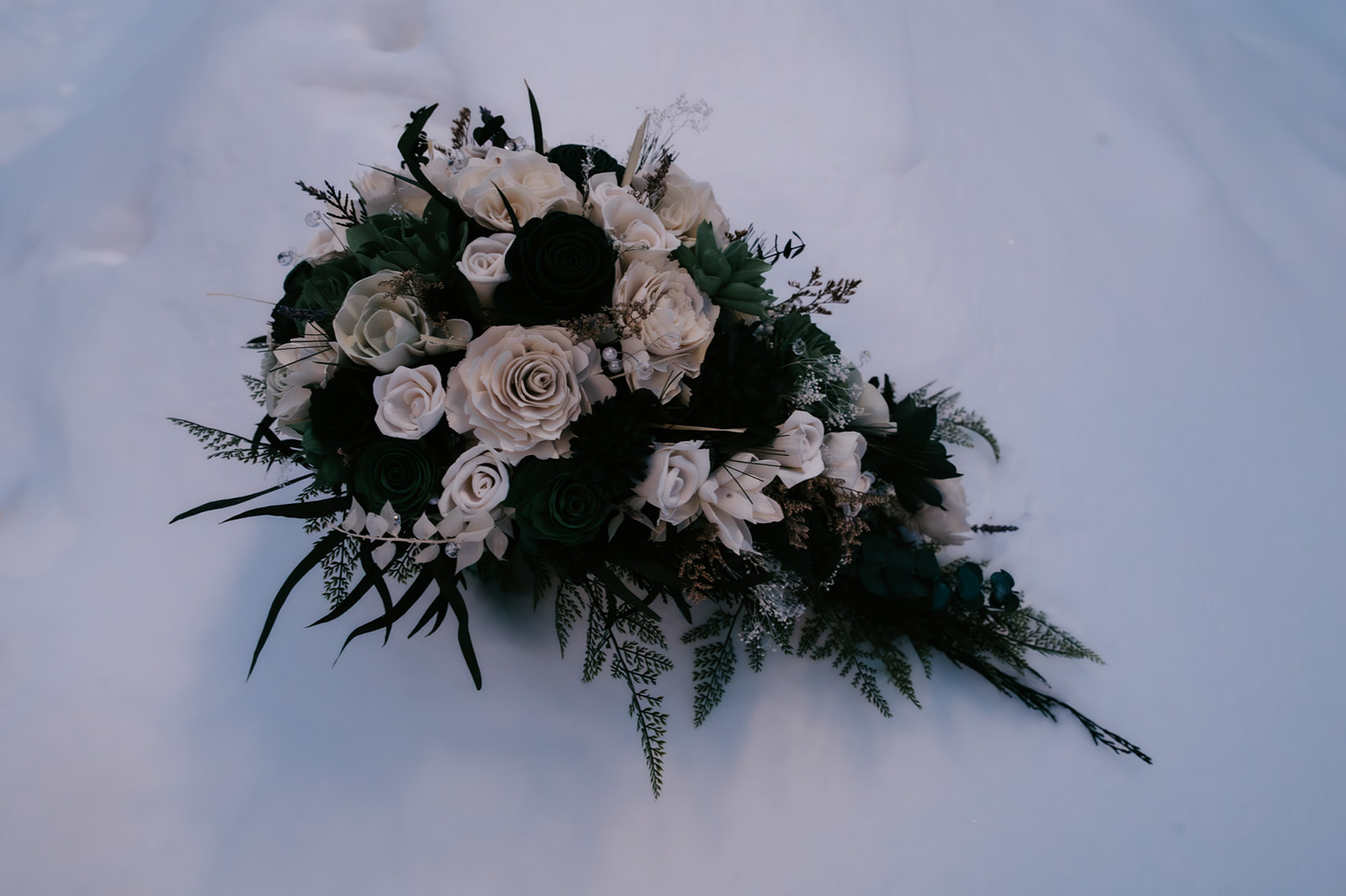 Cascading bouquet of white and deep green roses resting in the snow, featured in their Yellowstone elopement video.