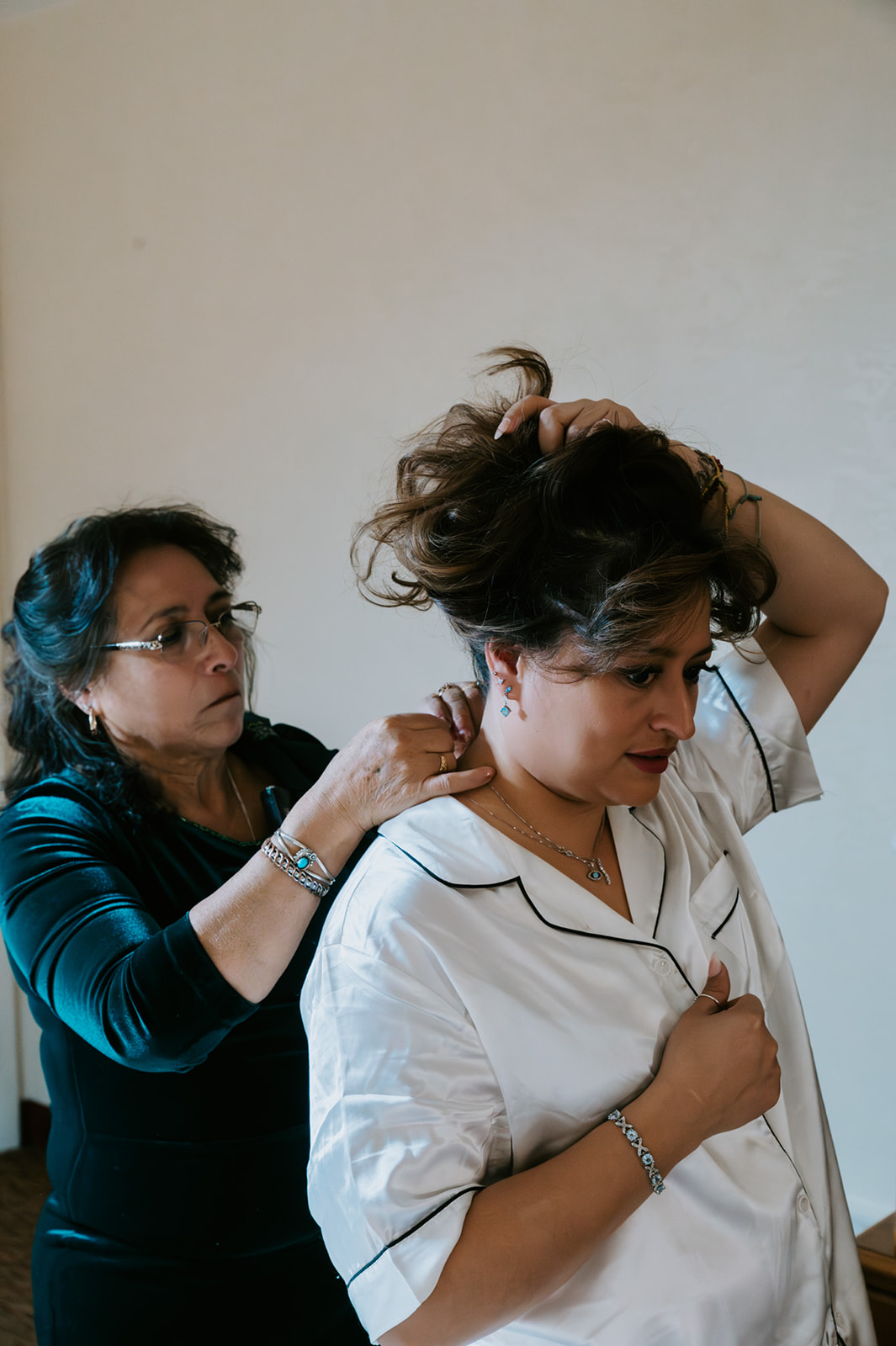 Mother adjusting the bride’s necklace as she finishes getting ready in soft window light.