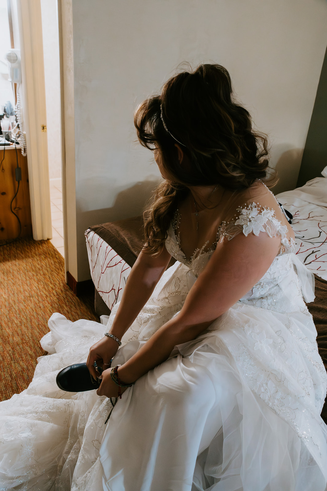 Bride sitting on a hotel bed fastening her shoes, captured during the quiet getting-ready moments of her winter elopement video.