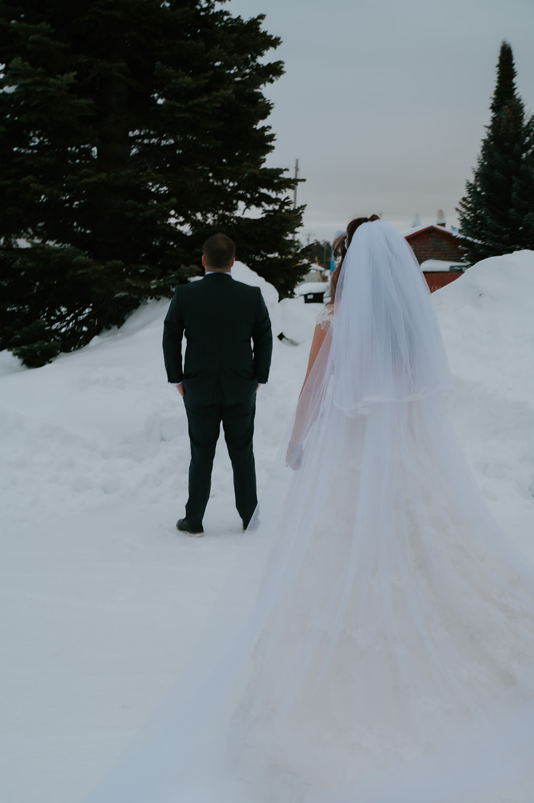 Back view of the bride walking through deep snow toward her groom during their intimate elopement video first look.