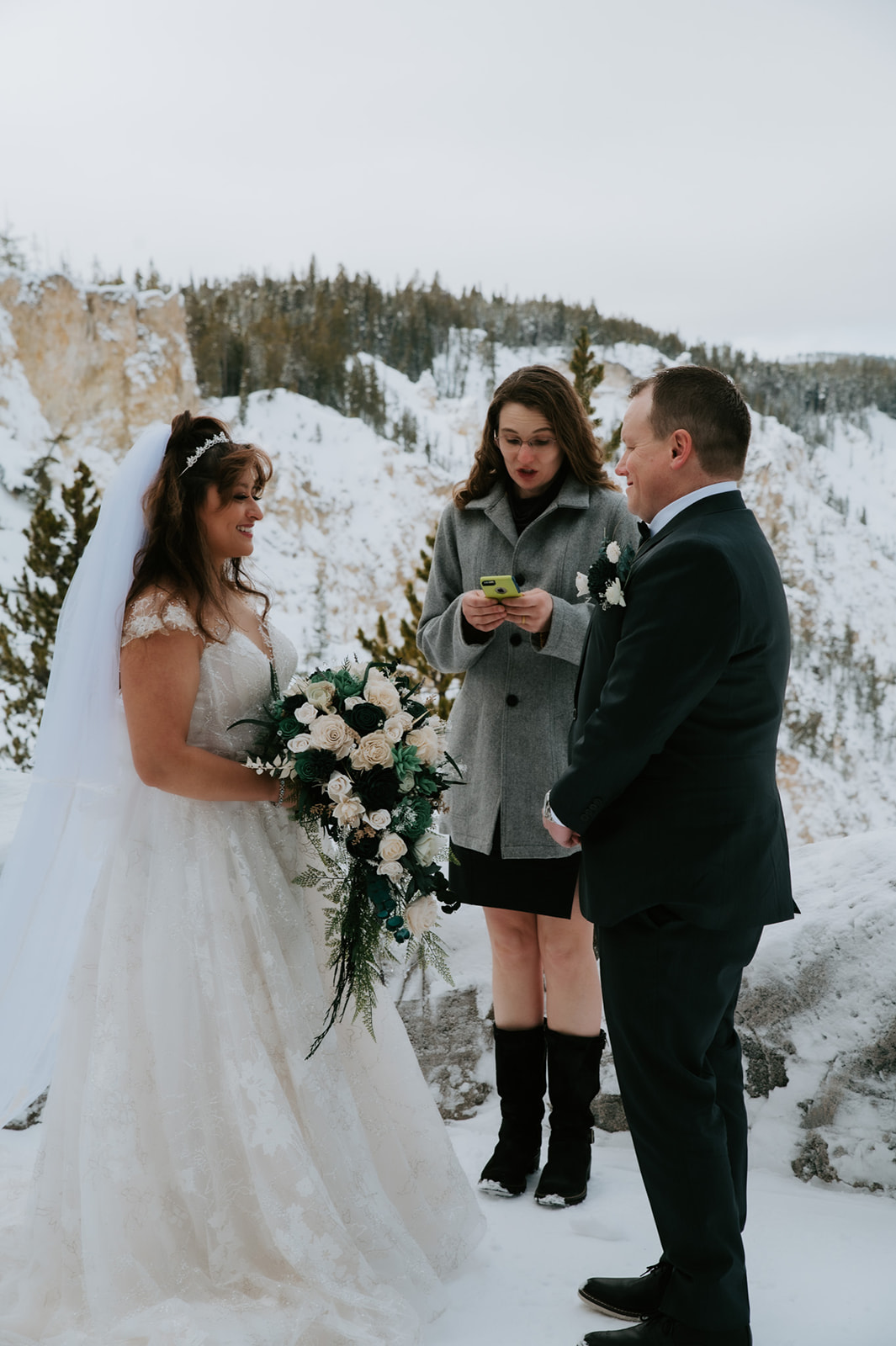 Bride and groom standing in the snow beside a white Yellowstone shuttle bus, bouquet cascading over her arm.