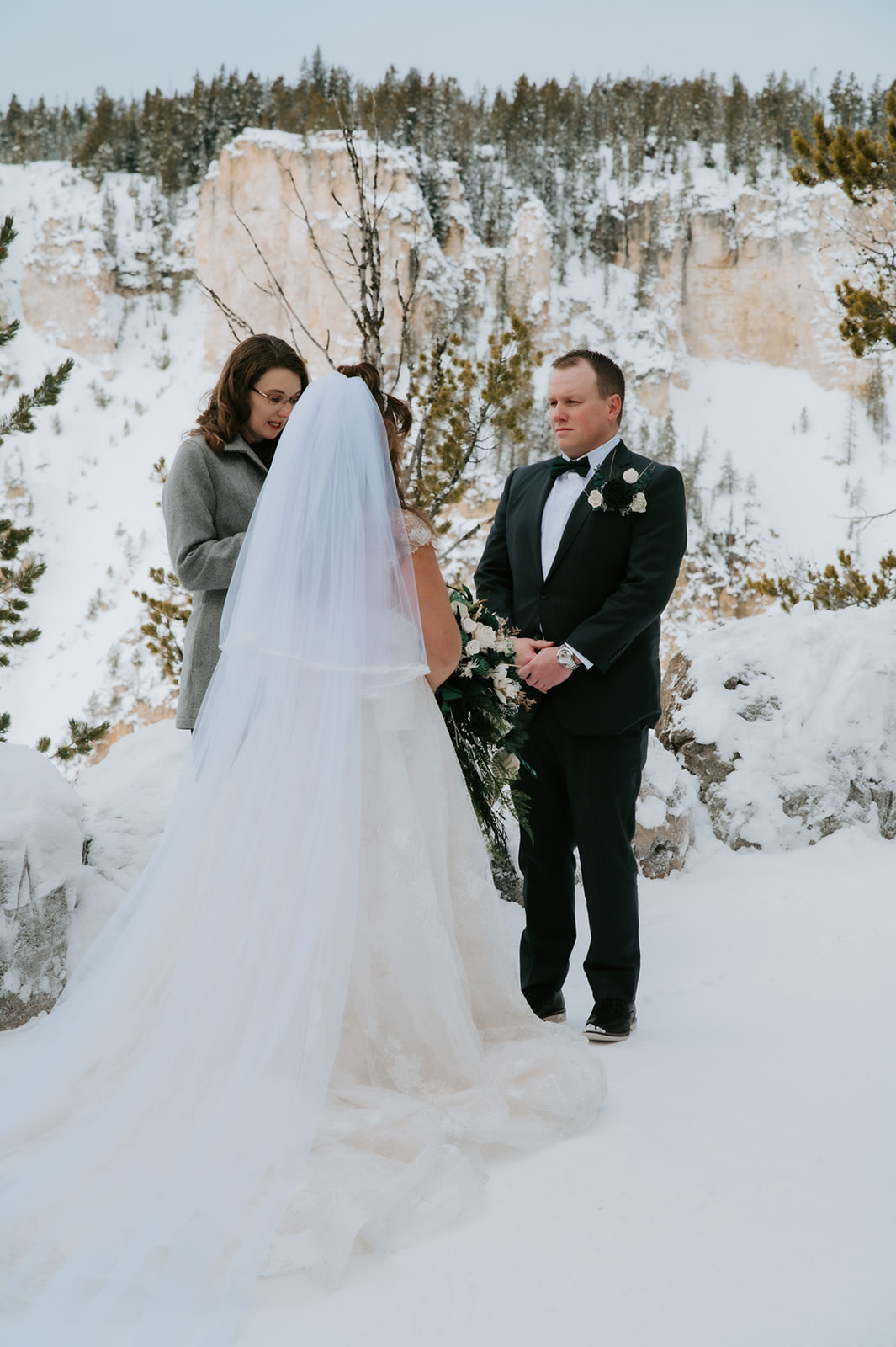 Officiant reading vows from her phone while the couple smiles during their Yellowstone winter elopement video ceremony.