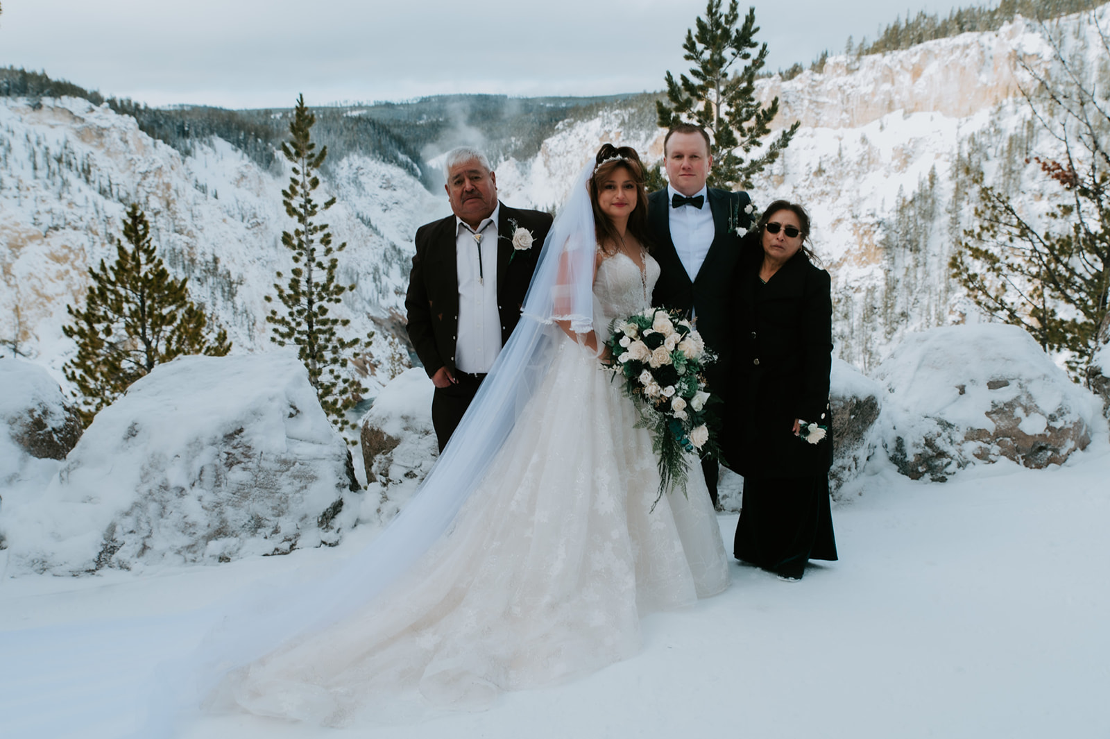 Bride and groom posing with family members at a snowy canyon overlook during their intimate winter elopement video in Yellowstone.