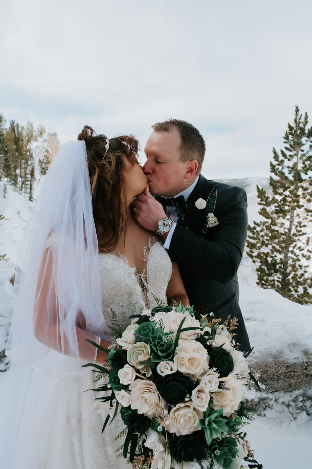 Bride and groom sharing a kiss in the snow with evergreen trees behind them, captured during their romantic winter elopement video.