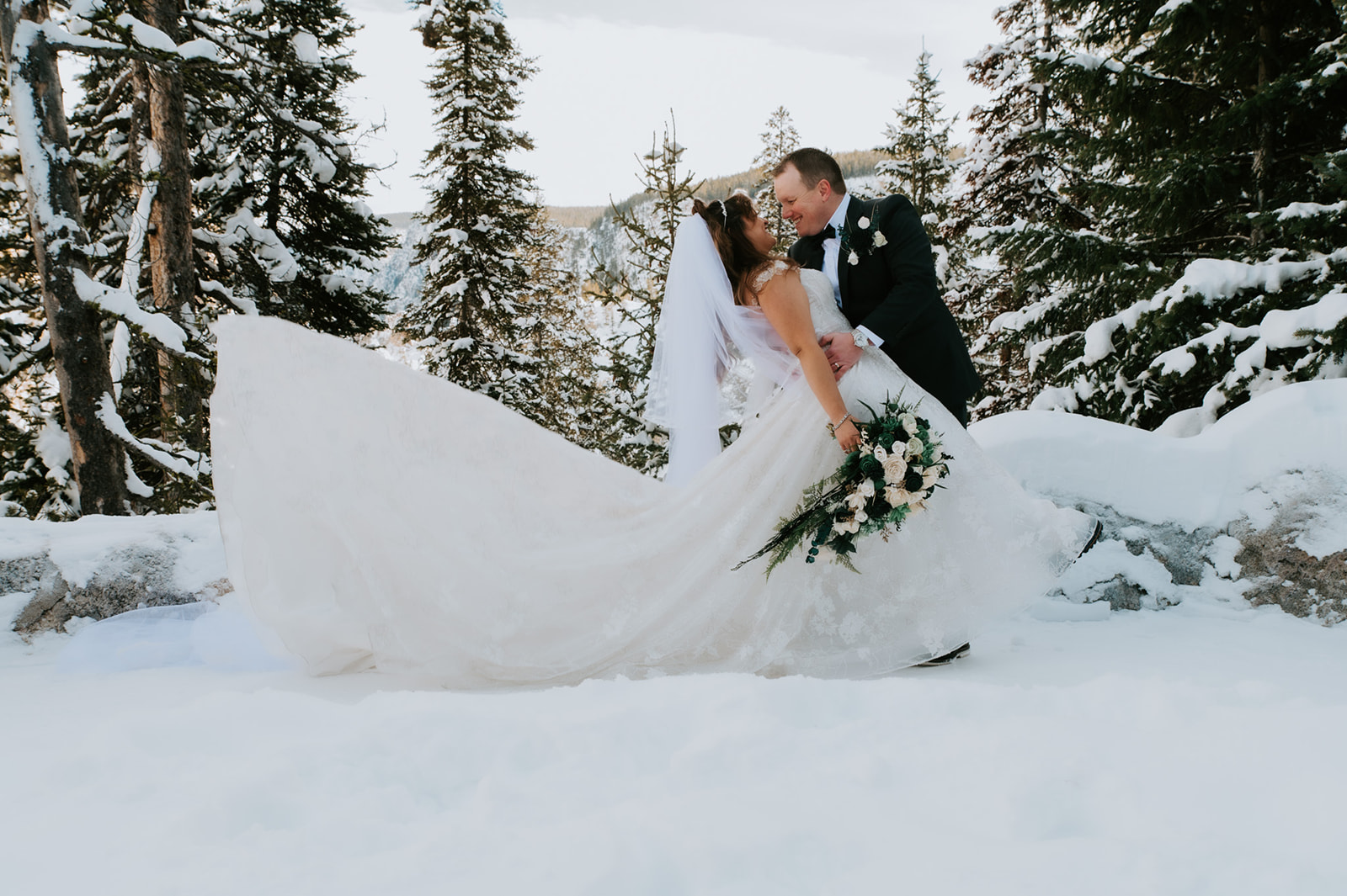 Groom dipping the bride in the snow as her long veil fans out behind her, a playful moment from their winter elopement video.
