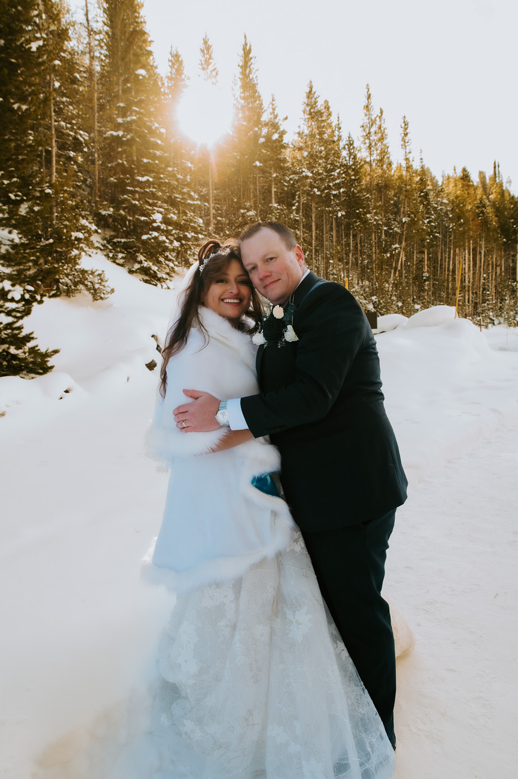 Newlyweds embracing in golden winter sunlight surrounded by snow-covered pine trees, captured for their Yellowstone elopement video.