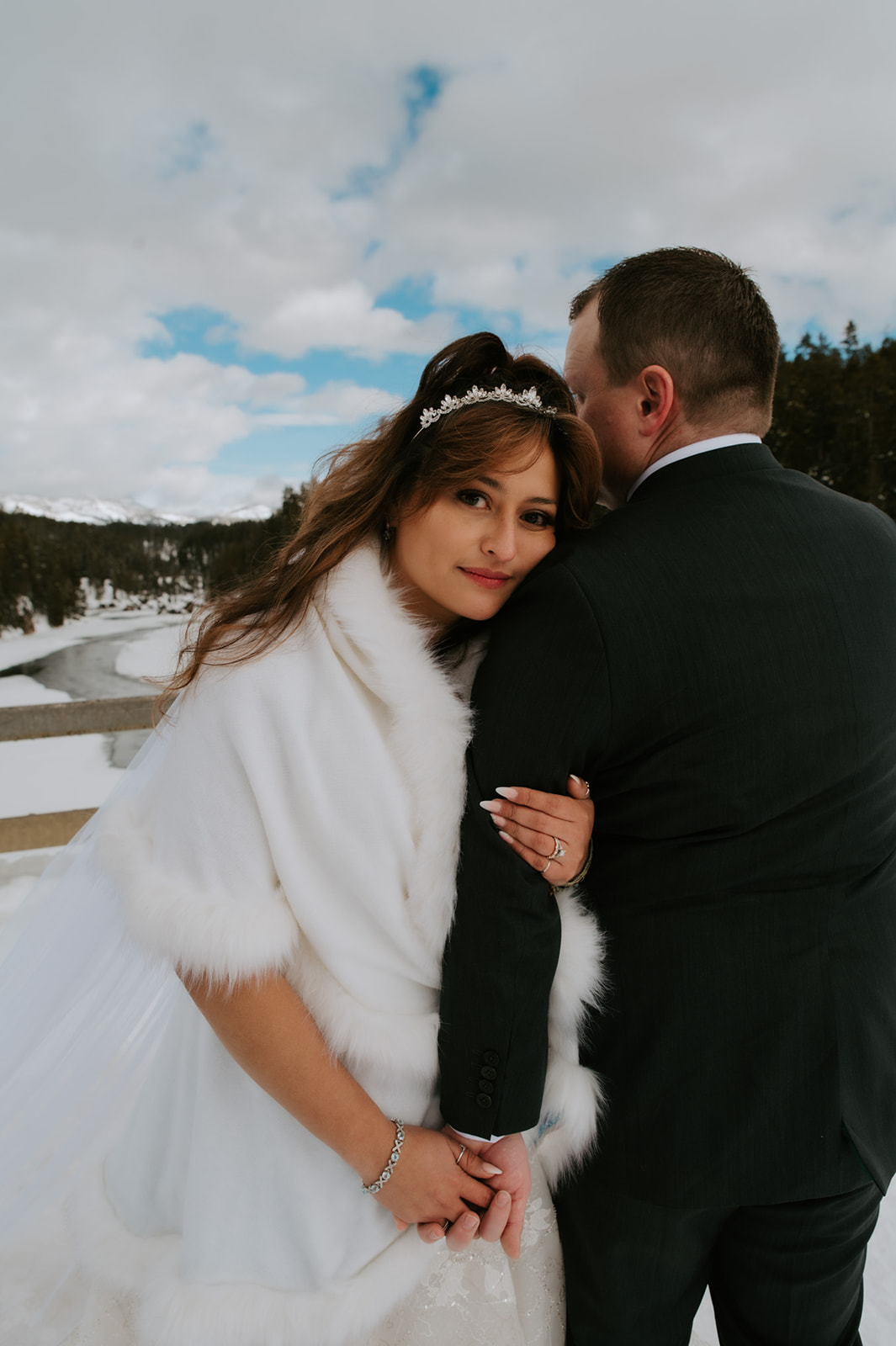 Bride looking back toward the camera while holding her groom’s arm on a snowy overlook, captured for their intimate elopement video.