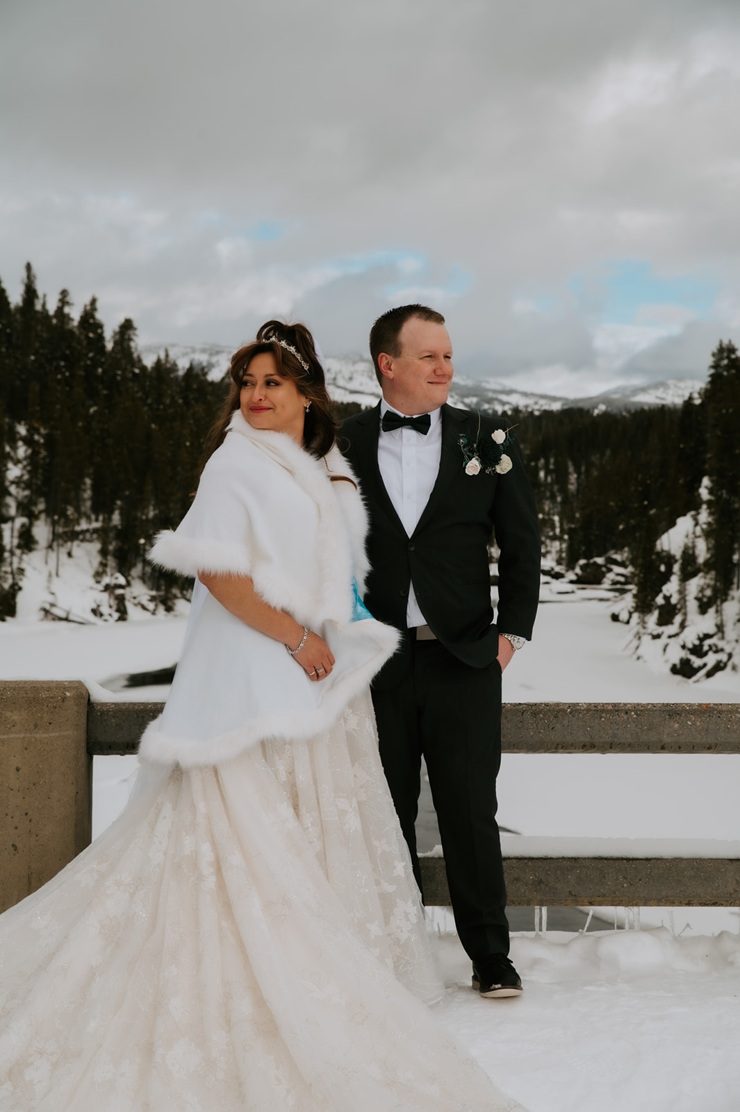 Bride and groom standing on a snowy bridge overlooking a frozen river and mountain landscape during their winter elopement video.