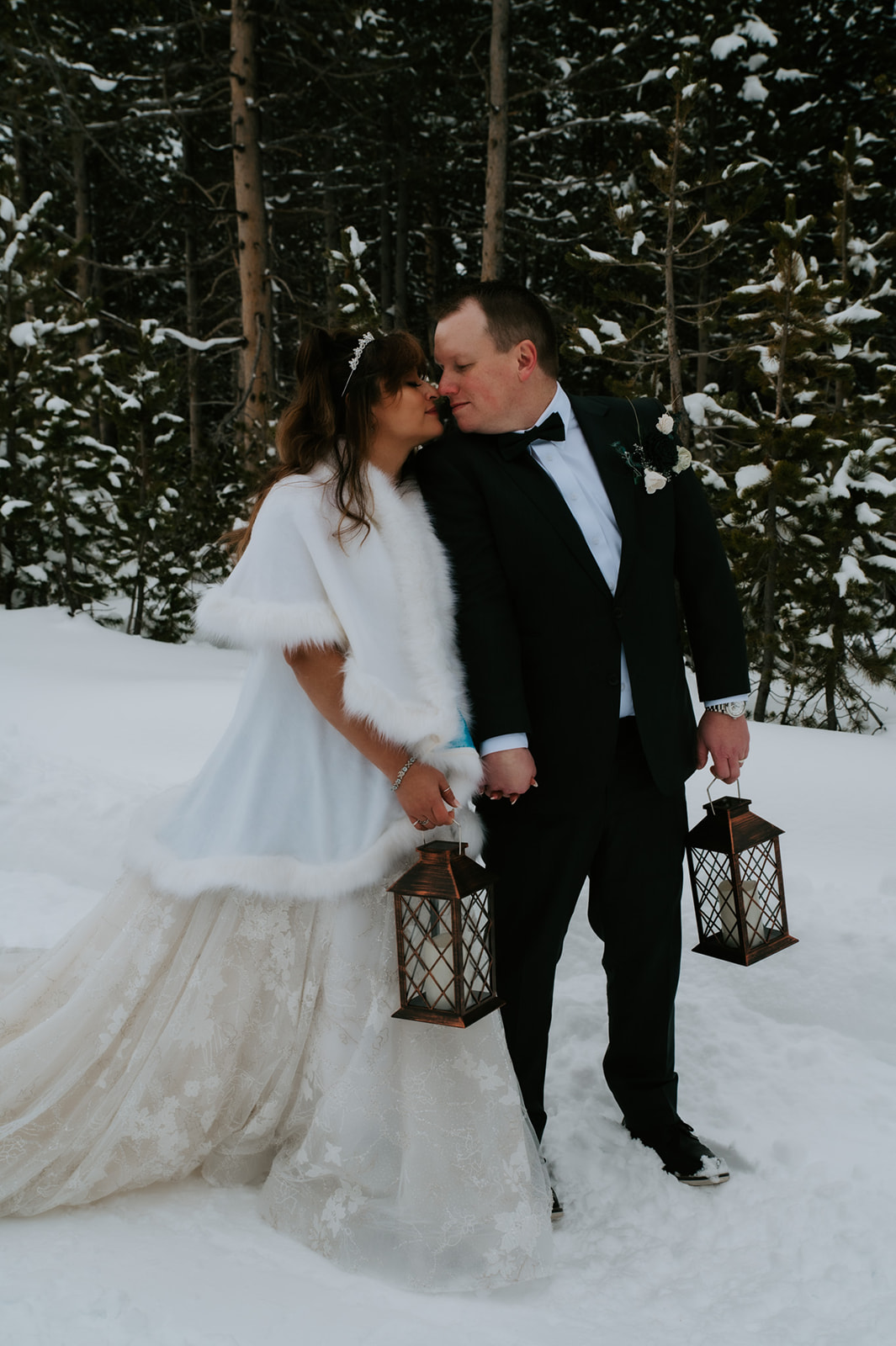 Bride and groom walking through snowy woods holding lanterns, featured in their cozy winter elopement video.