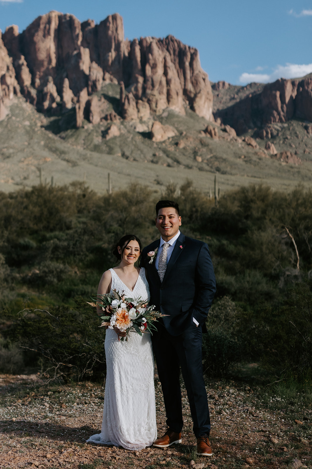 Arizona elopement portrait of bride and groom smiling beneath towering desert mountains and clear blue sky