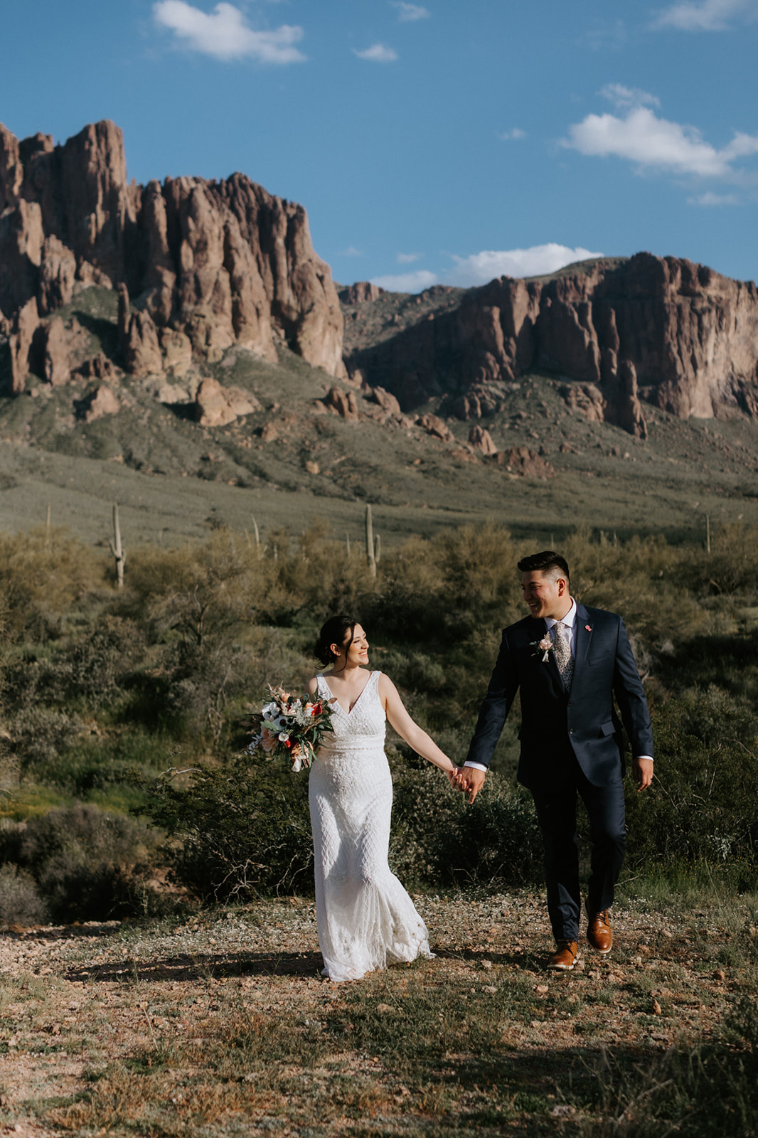Couple walking hand in hand through desert landscape with towering rock formations in the distance