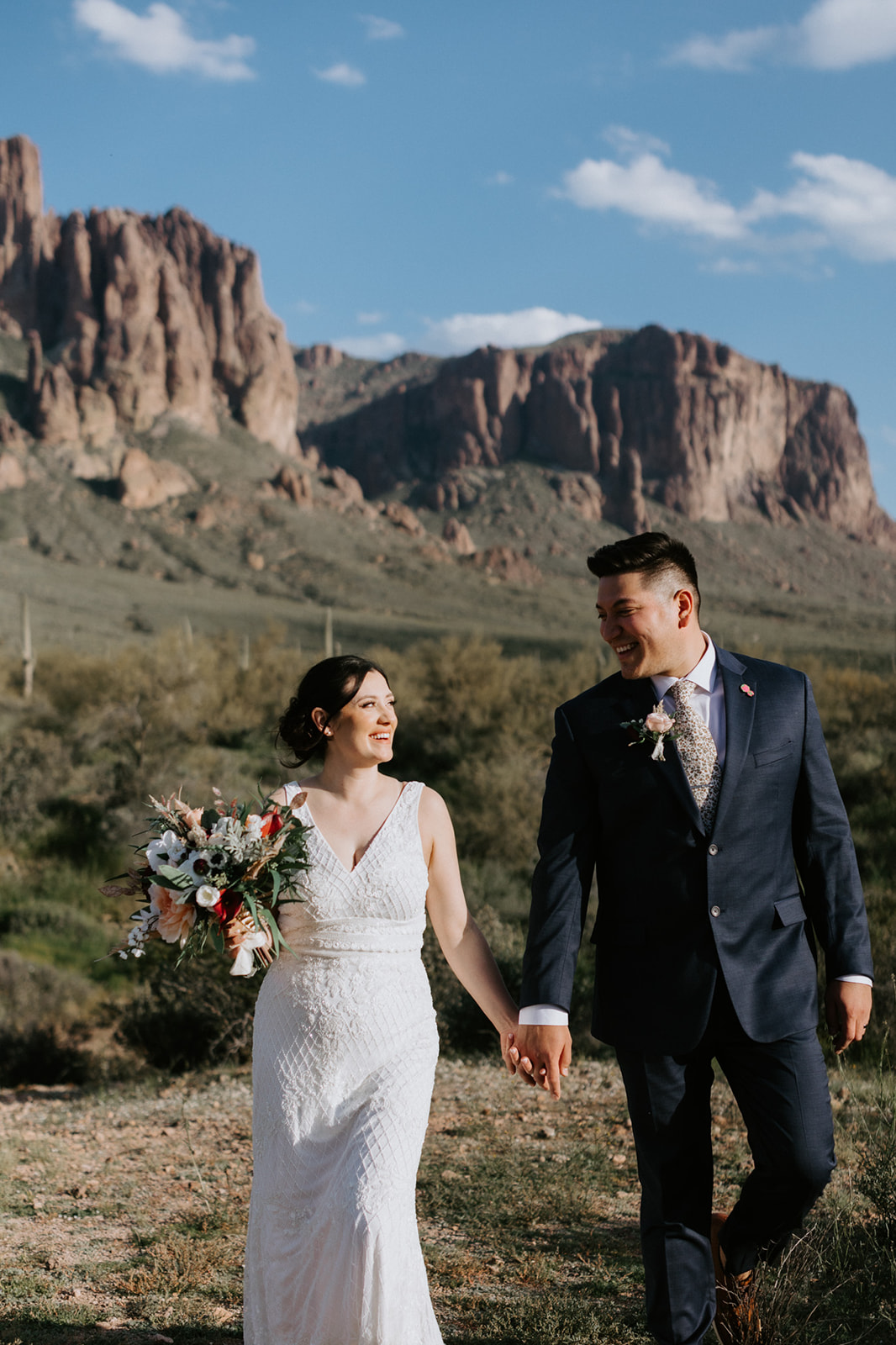 Bride and groom walking hand in hand during their Arizona elopement with desert mountains rising behind them