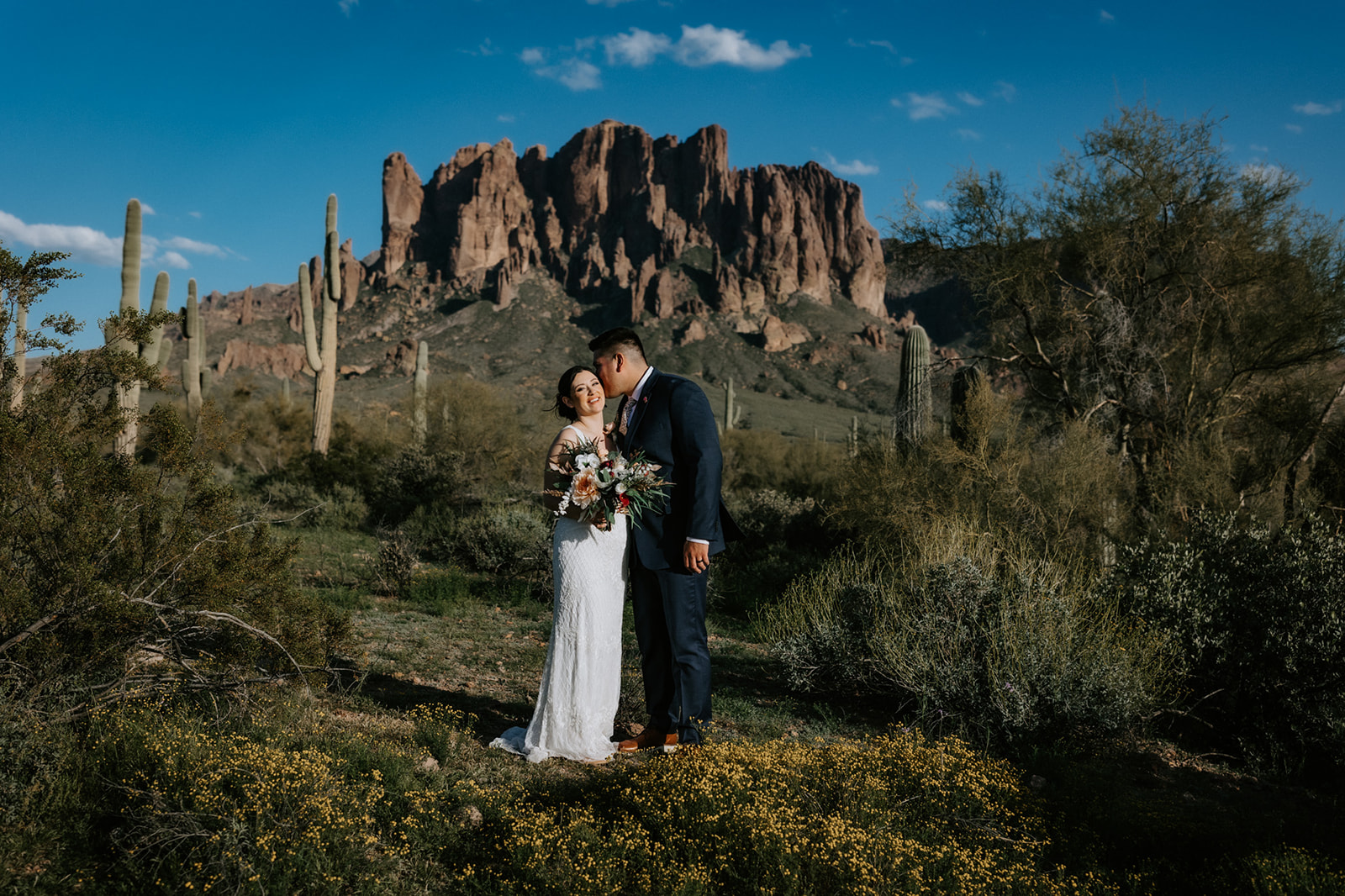 Arizona elopement in the desert with couple surrounded by wildflowers and saguaro cacti beneath dramatic cliffs