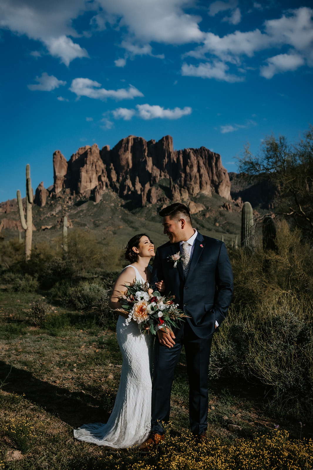 Arizona elopement portrait beneath towering desert mountains with saguaro cacti and wildflowers