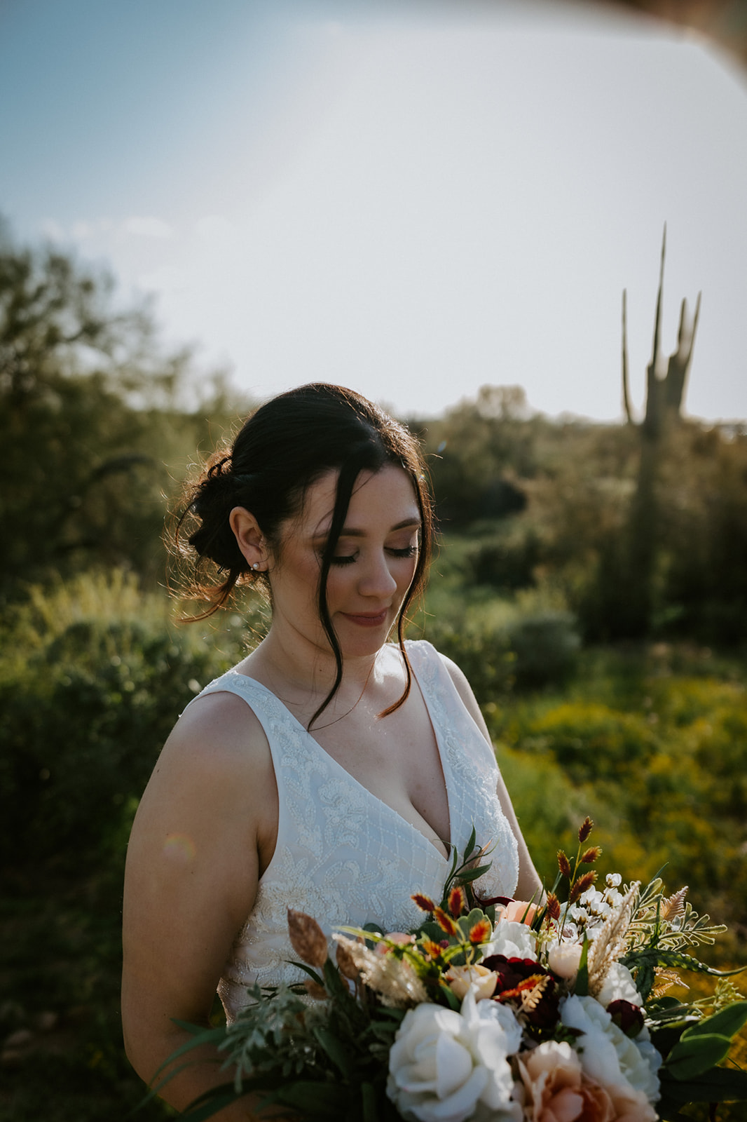 Close-up of bride holding bouquet in soft sunset light with desert greenery behind her