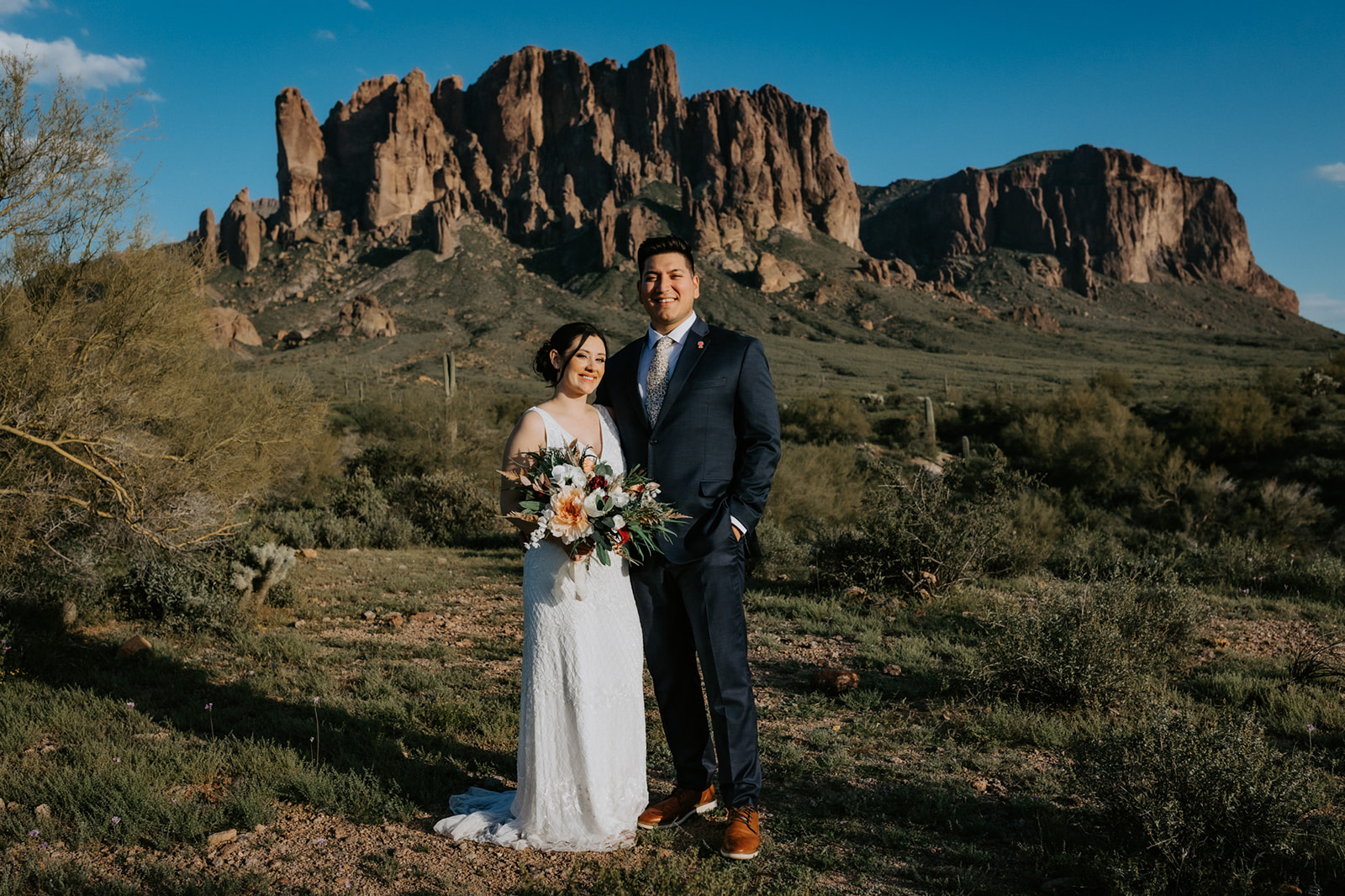Bride and groom standing together in the desert with dramatic mountain backdrop and clear blue sky