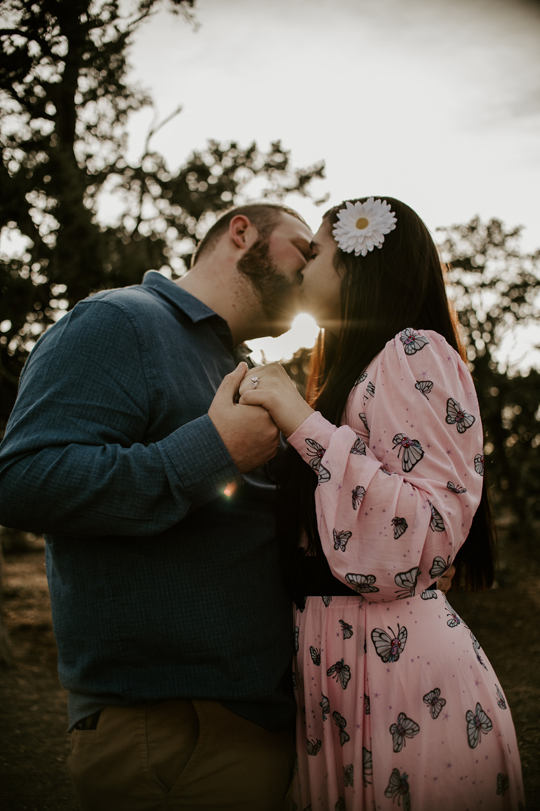 Arizona elopement kiss at sunset with sun flare peeking through trees as couple holds hands