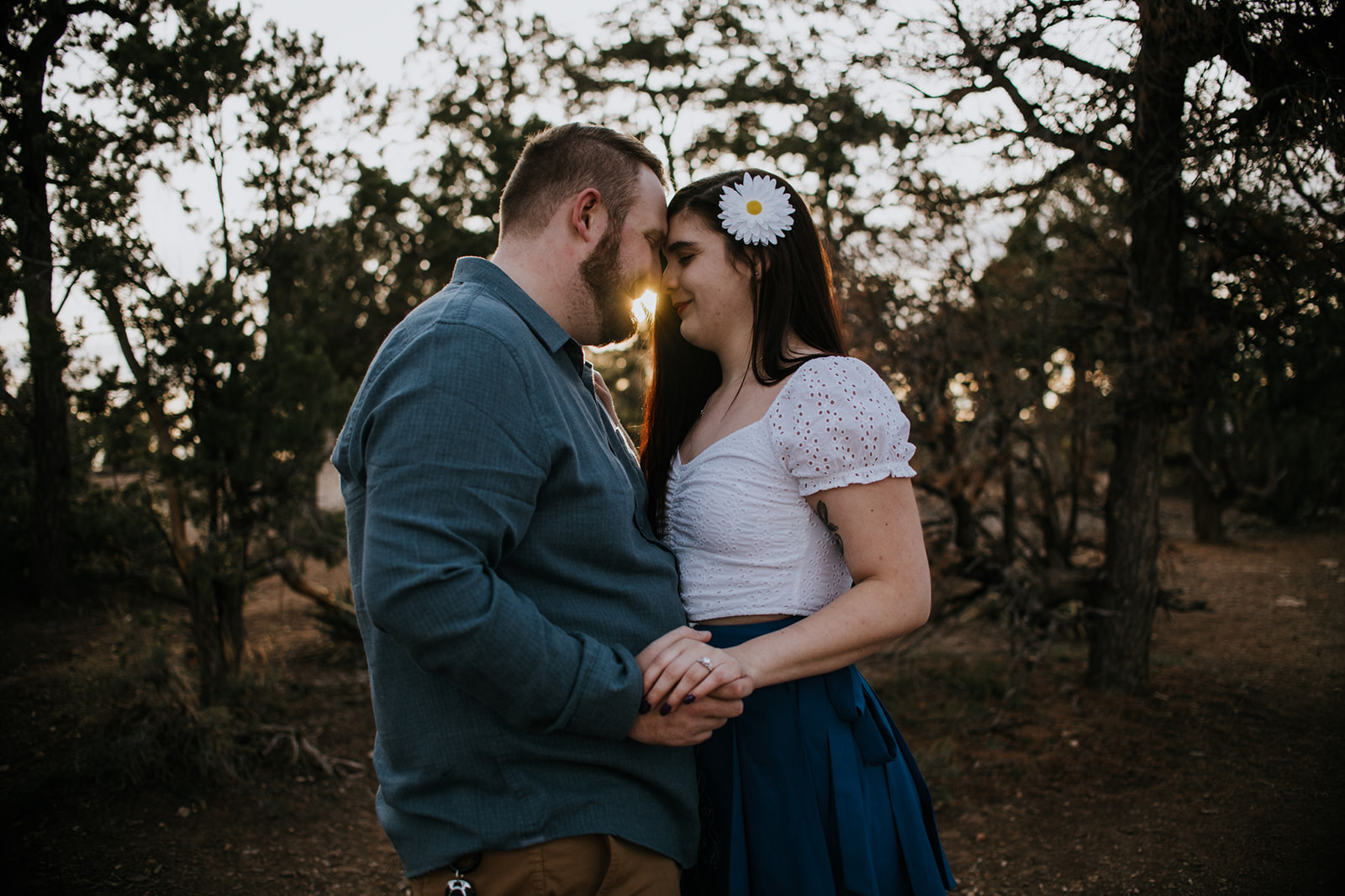 Golden hour portrait of couple holding each other in a wooded clearing with sun flaring through trees