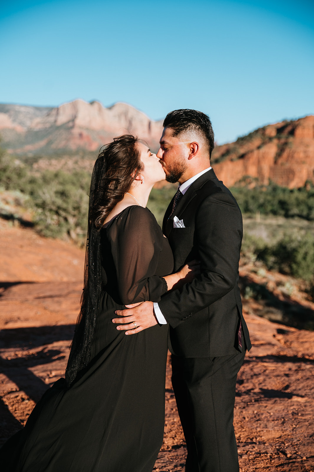 Arizona elopement at golden hour in Sedona with couple kissing on red rock overlook under clear blue sky
