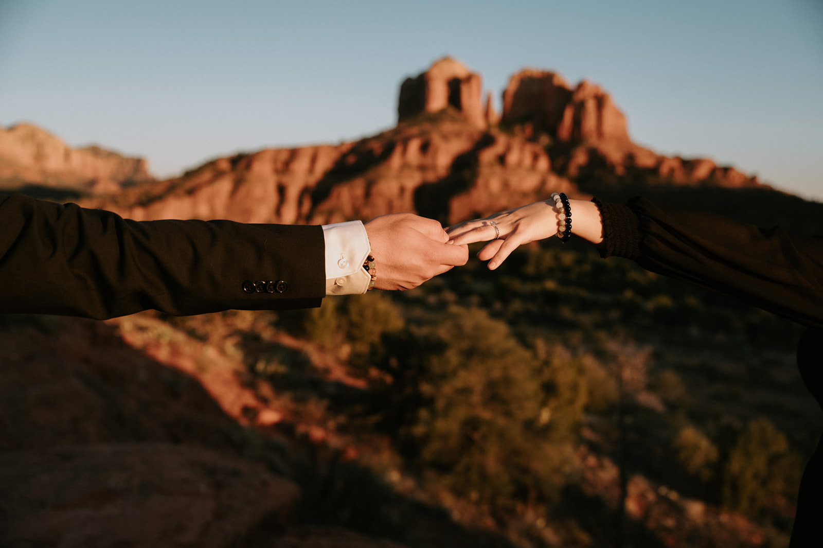 Close-up of hands reaching together with red rock formations softly blurred in the background at sunset