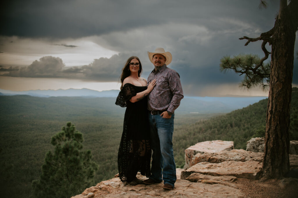 Couple standing on a cliffside overlook with dramatic monsoon clouds rolling across a forested valley
