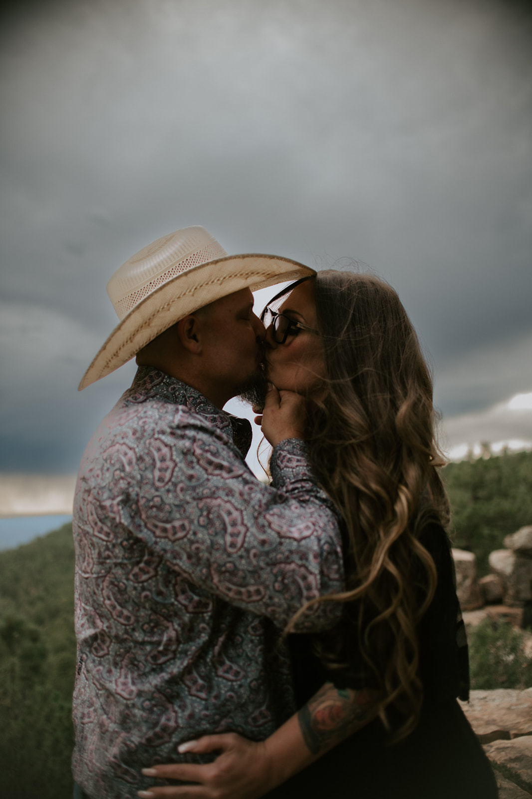Arizona elopement couple kissing on a cliffside overlook beneath dark storm clouds in northern Arizona