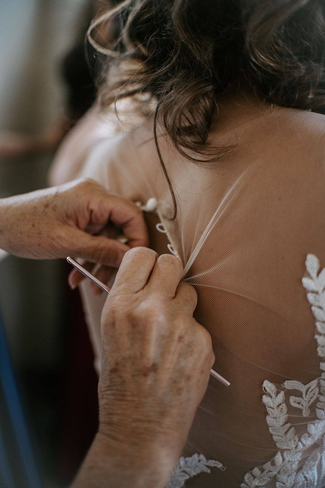 Close-up of hands fastening the back of a lace wedding dress during getting ready moments
