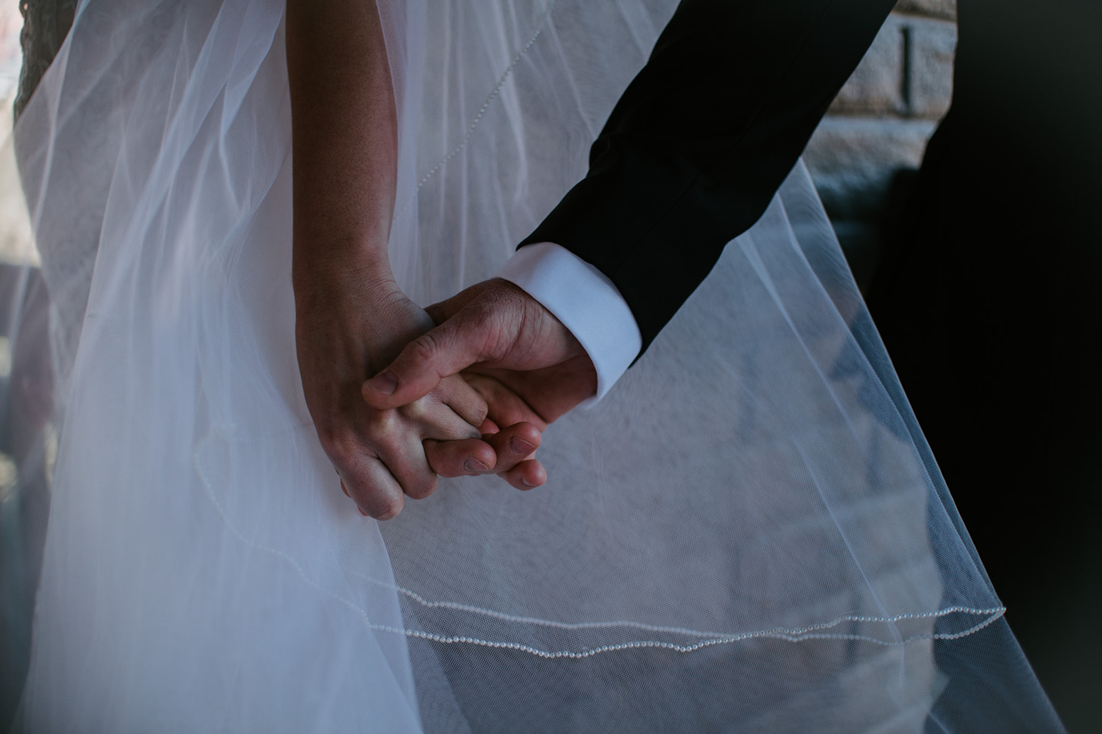 Close-up of couple holding hands with veil flowing softly during an elopement in Arizona
