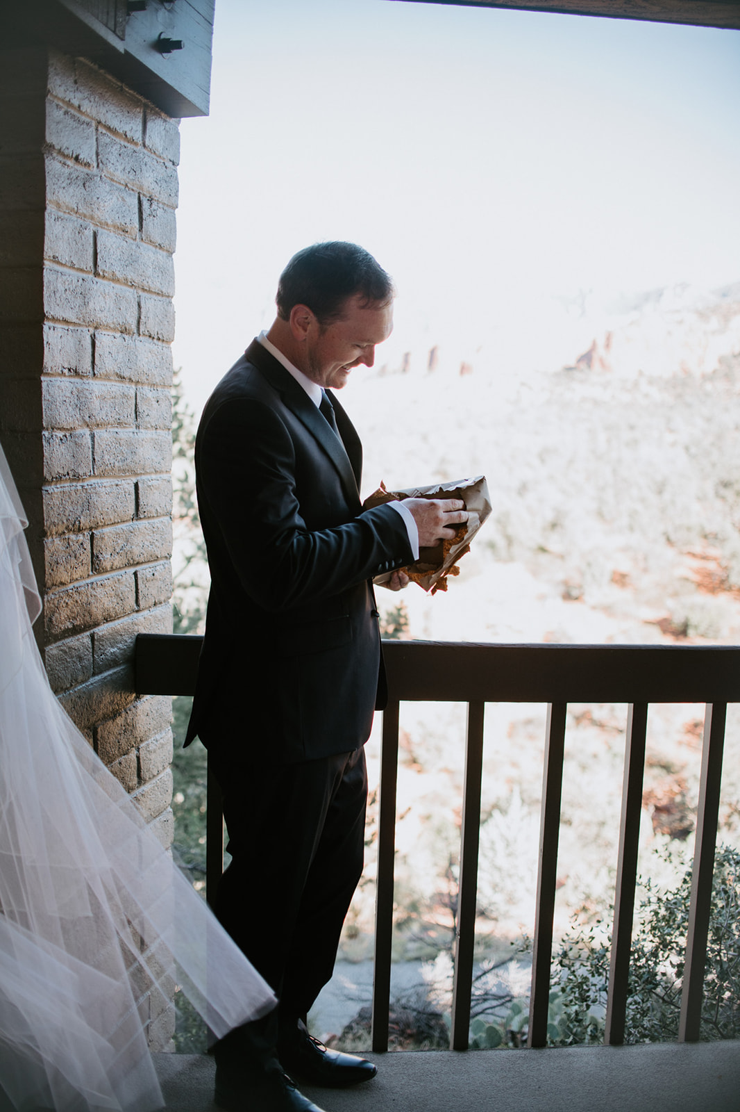 Groom opening a small gift on a balcony with soft natural light before their elopement in Arizona
