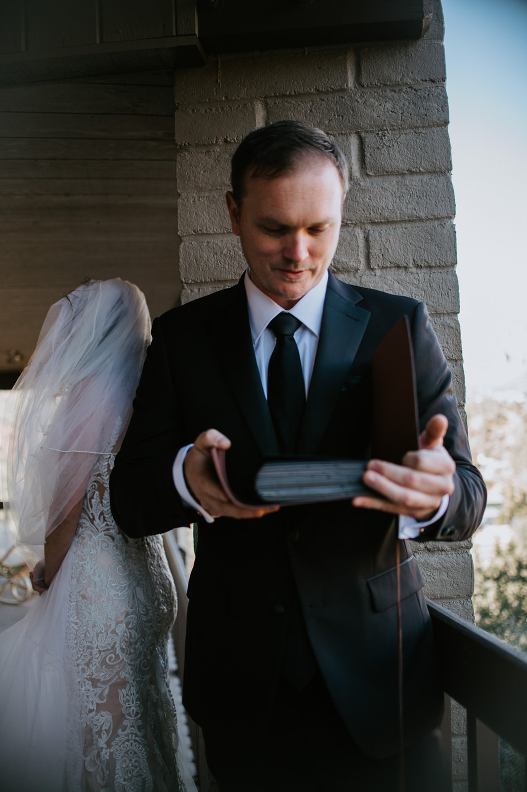 Groom opening a keepsake box while standing on a balcony with desert views