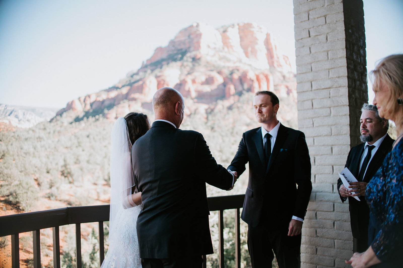 Couple exchanging a handshake during a small balcony ceremony with Sedona red rock views during their elopement in Arizona

