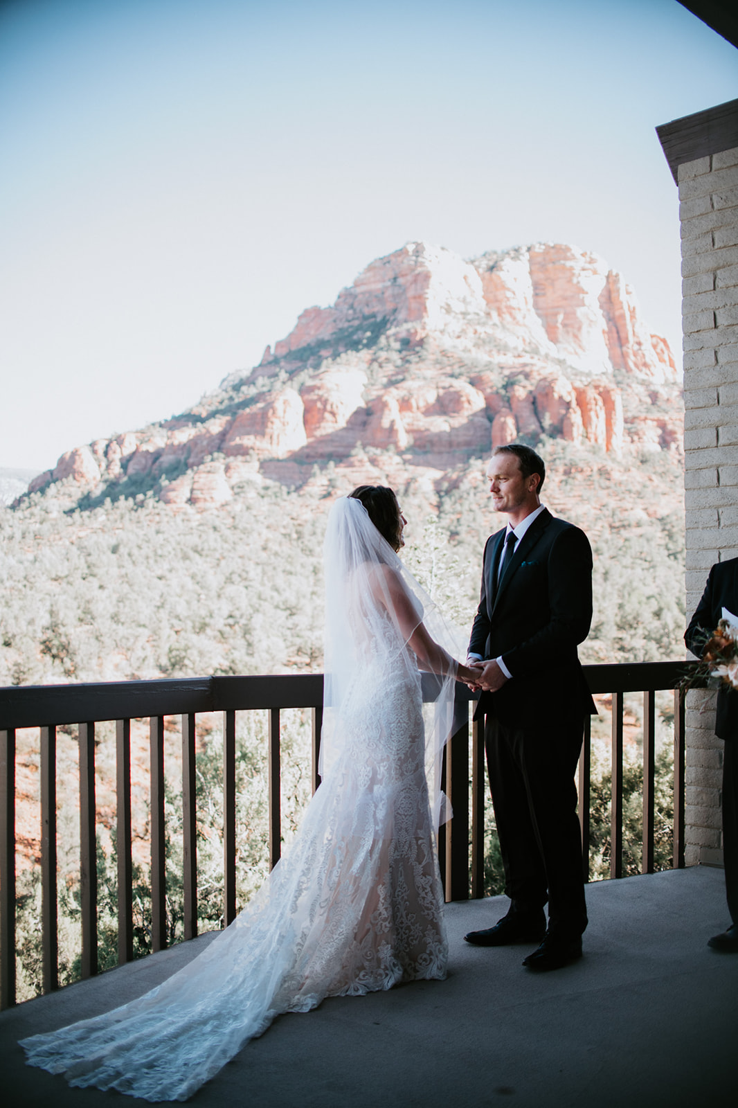 Bride and groom holding hands on a balcony overlooking Sedona red rocks during an intimate elopement in Arizona
