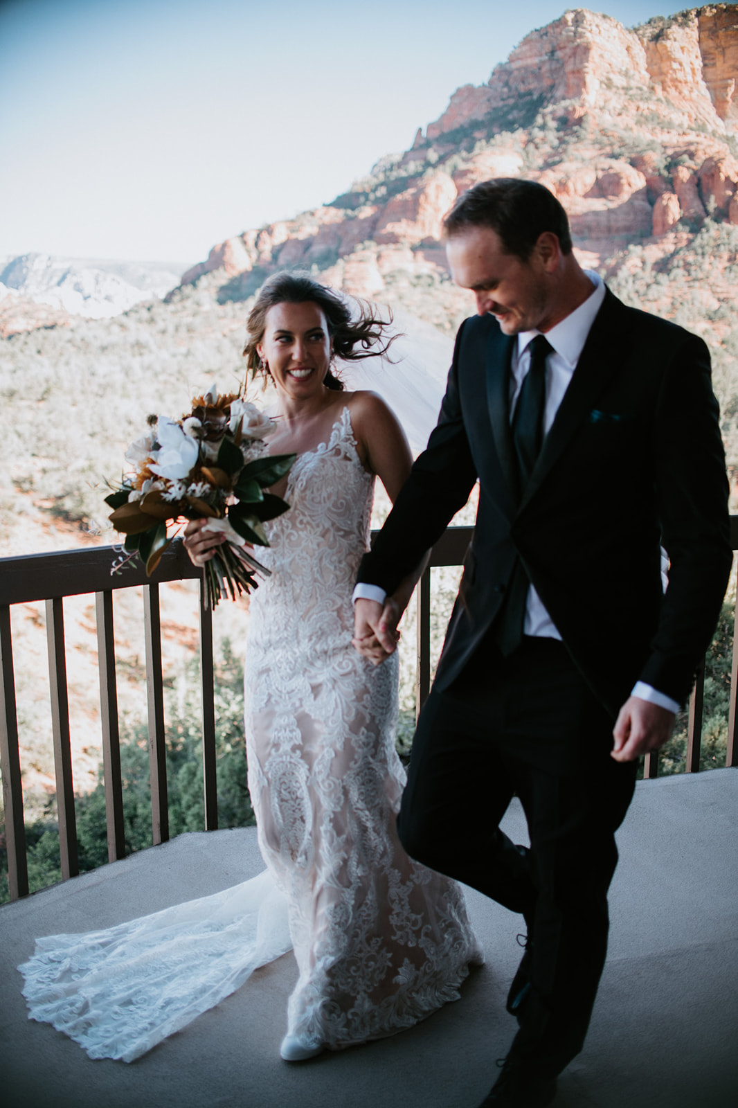 Bride and groom walking hand in hand along a Sedona Airbnb balcony after their ceremony

