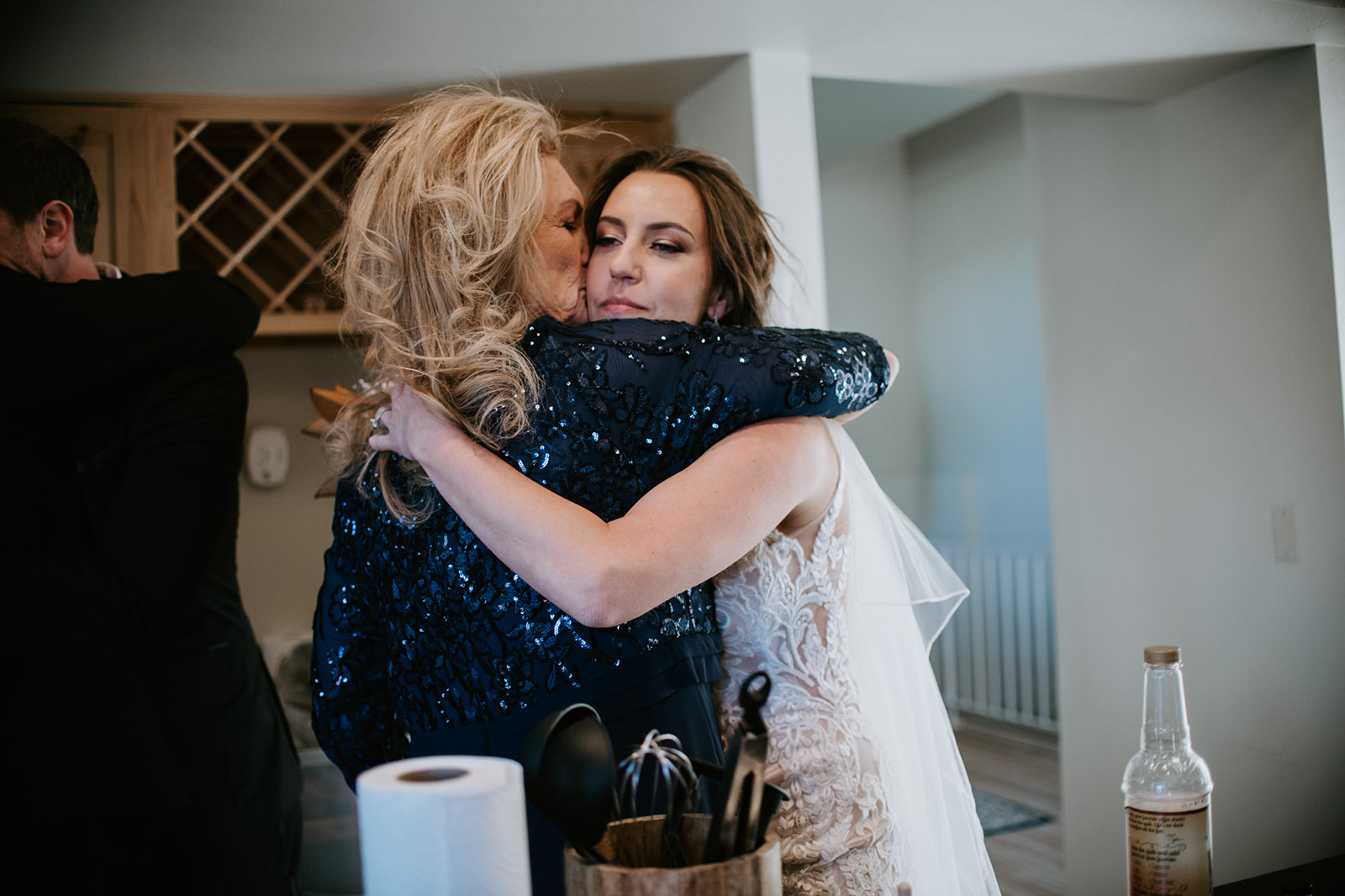 Bride sharing an emotional hug with a family member inside an Airbnb kitchen after the ceremony
