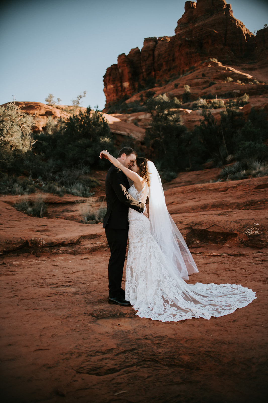 Bride and groom embracing on red rocks with warm desert light during their elopement in Arizona
