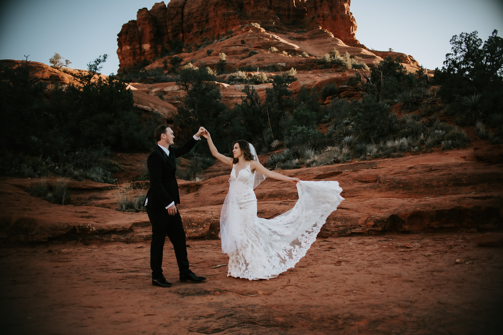 Couple dancing on Sedona red rocks with flowing wedding dress during an Arizona elopement
