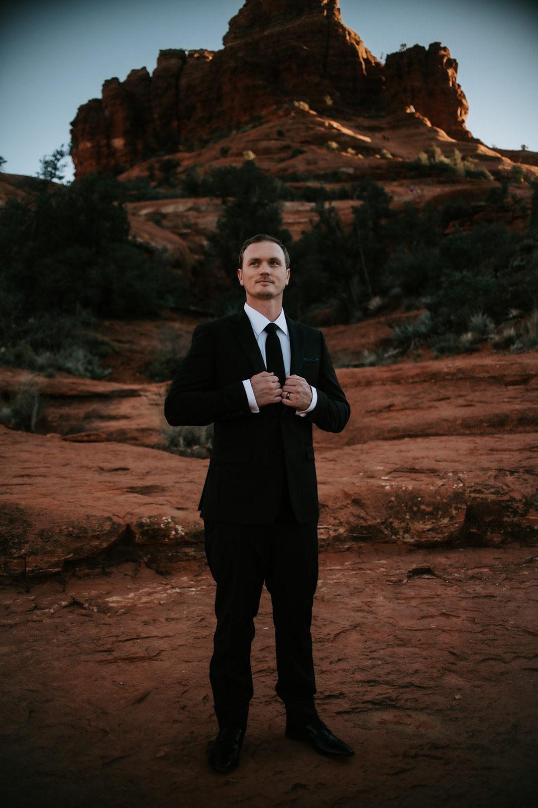 Groom adjusting suit jacket on Sedona red rocks before an Arizona elopement ceremony
