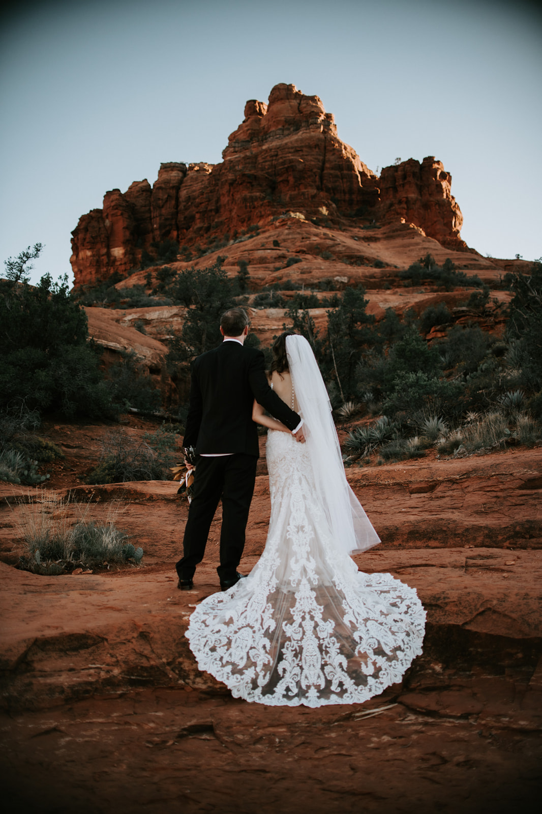 Bride and groom walking away together across Sedona red rocks after their ceremony