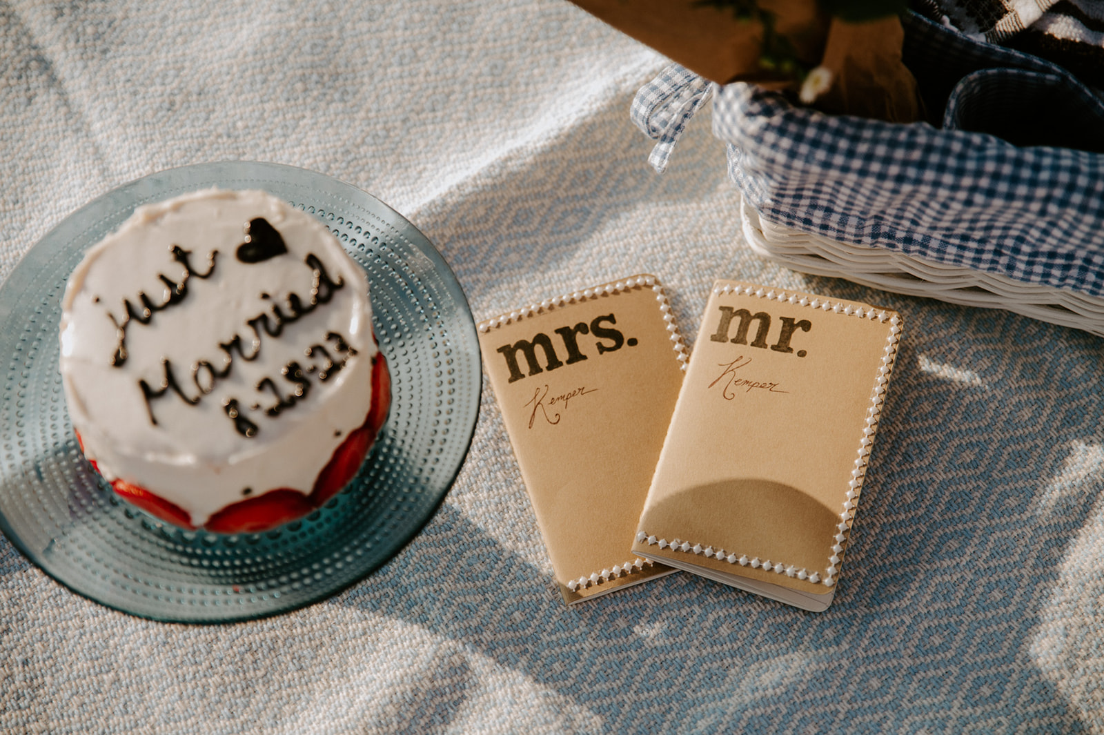 Small elopement cake and vow books laid out on a picnic blanket, simple details included in an elopement checklist.
