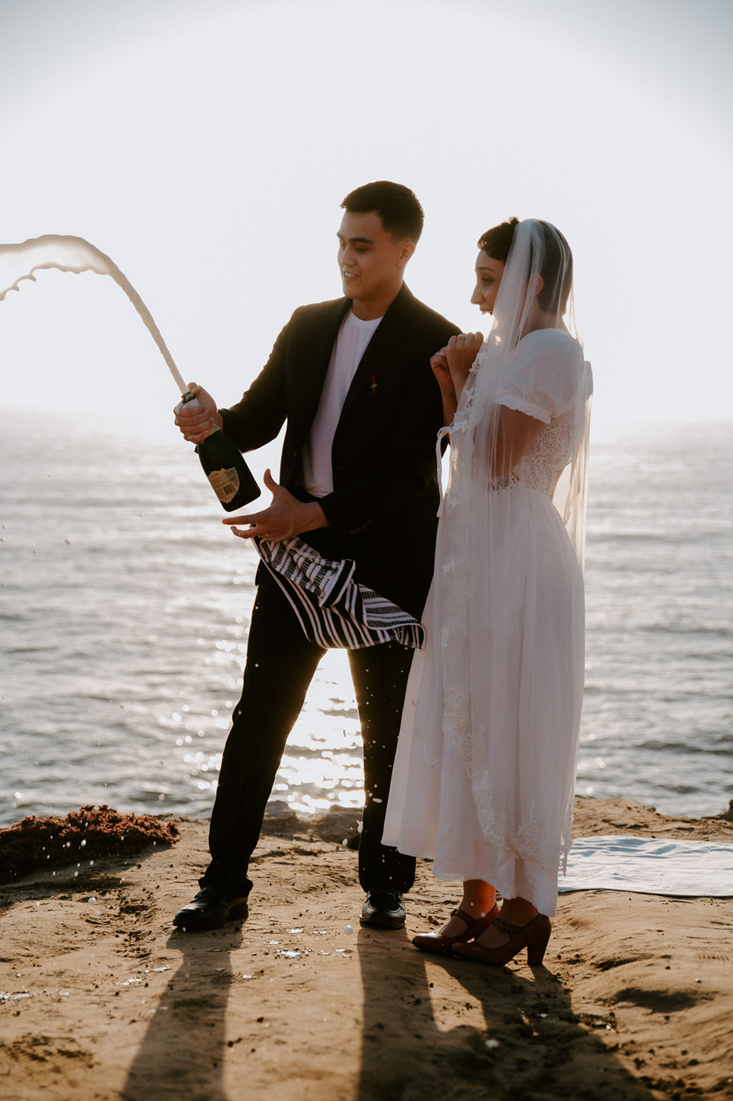 Champagne spraying into the air as the couple laughs on a seaside bluff, a playful detail to add to your elopement checklist.
