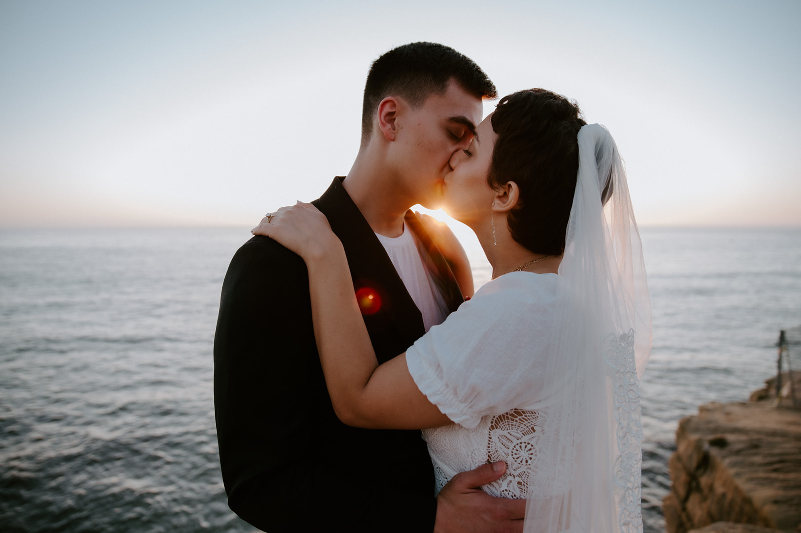 Bride and groom kissing with golden light reflecting off the ocean behind them, a romantic highlight from their elopement checklist.
