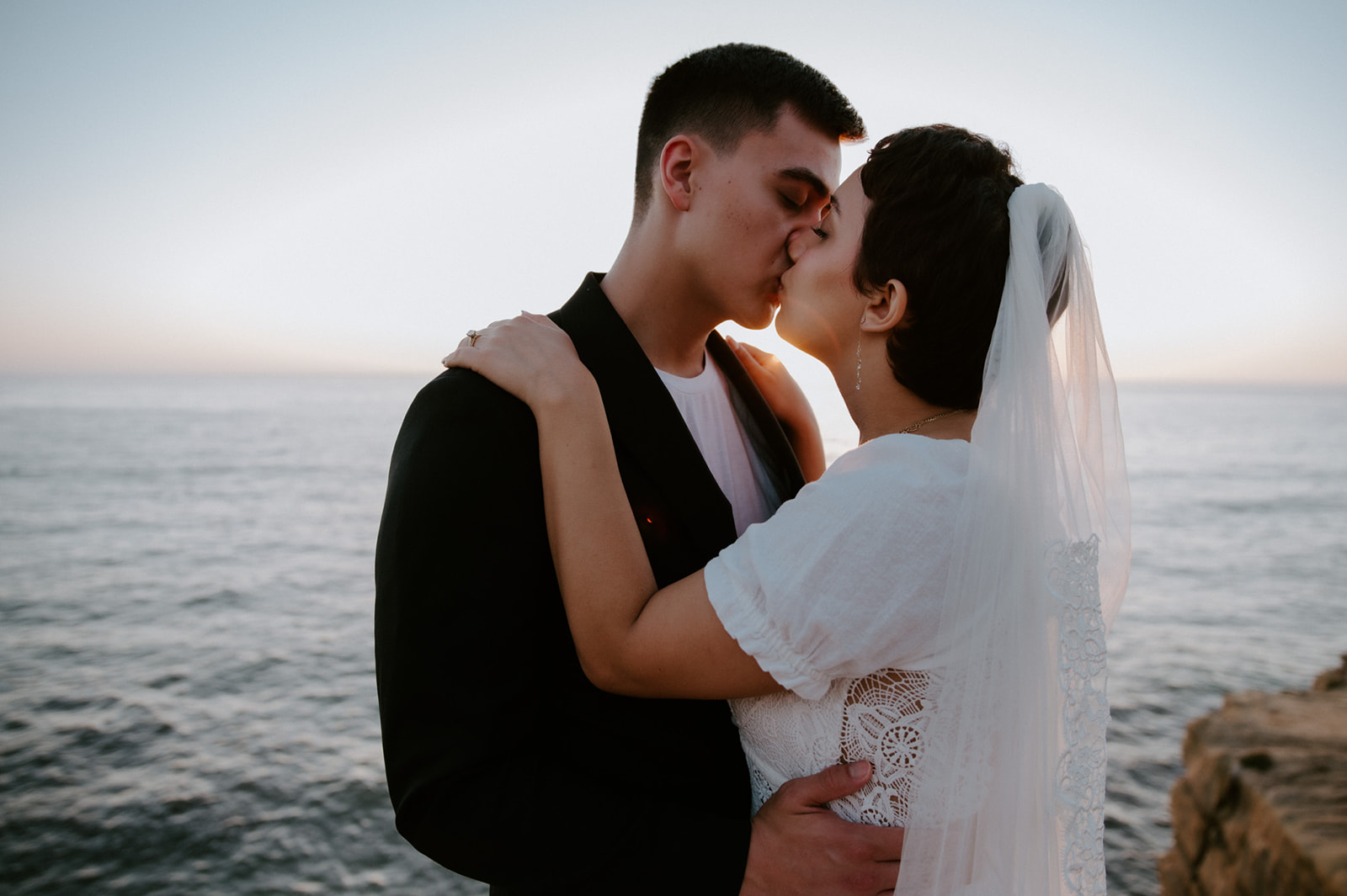 Close-up of couple kissing at sunset by the ocean, a soft and emotional moment from their elopement checklist.
