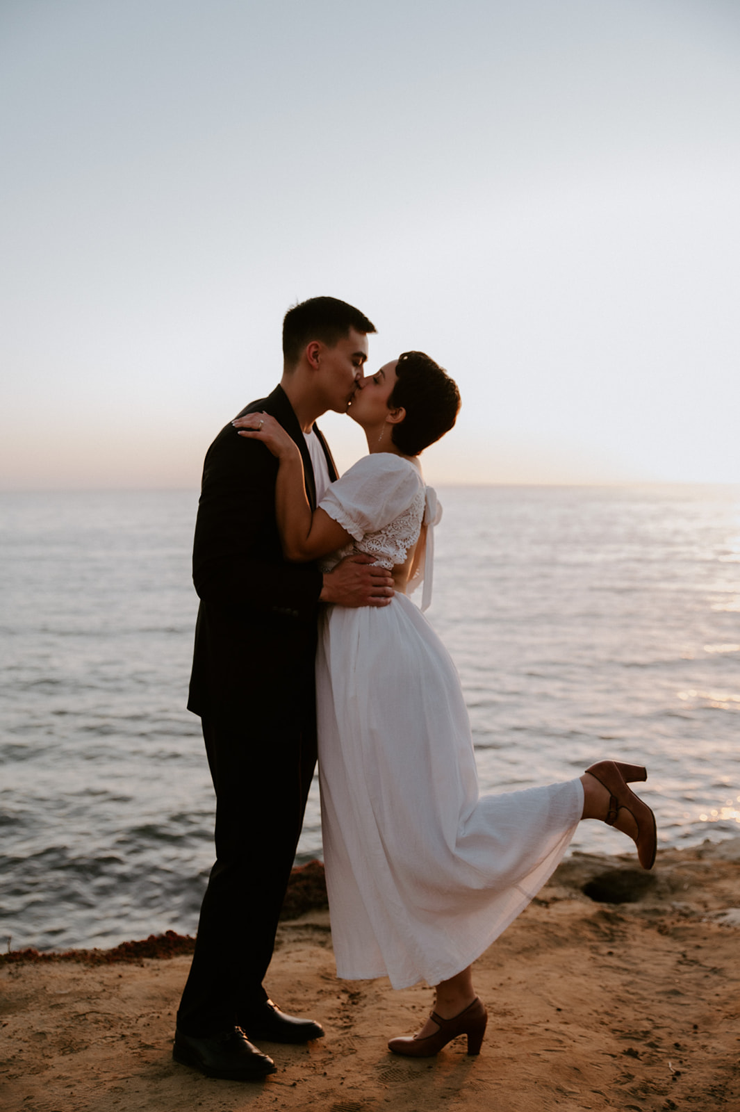 Couple kissing at sunset with the ocean behind them, capturing the emotion and freedom of an elopement checklist day.
