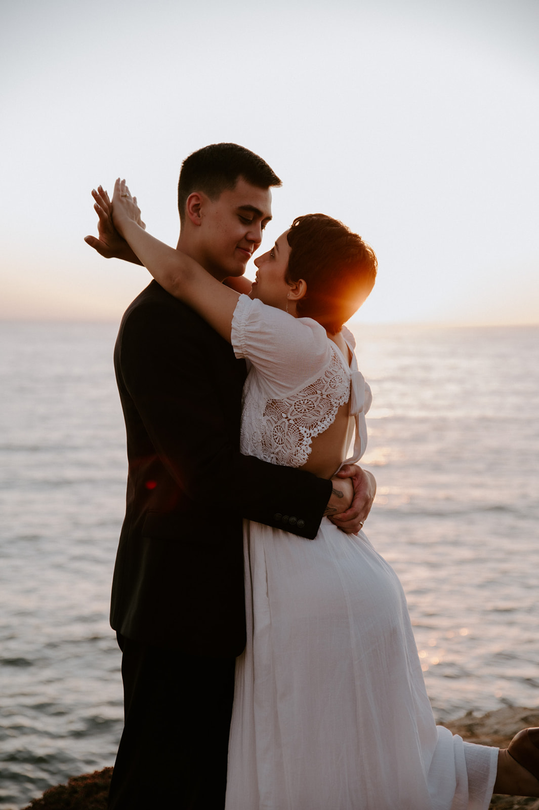 Couple embracing and smiling at each other in golden hour light by the ocean, a quiet connection during their elopement.
