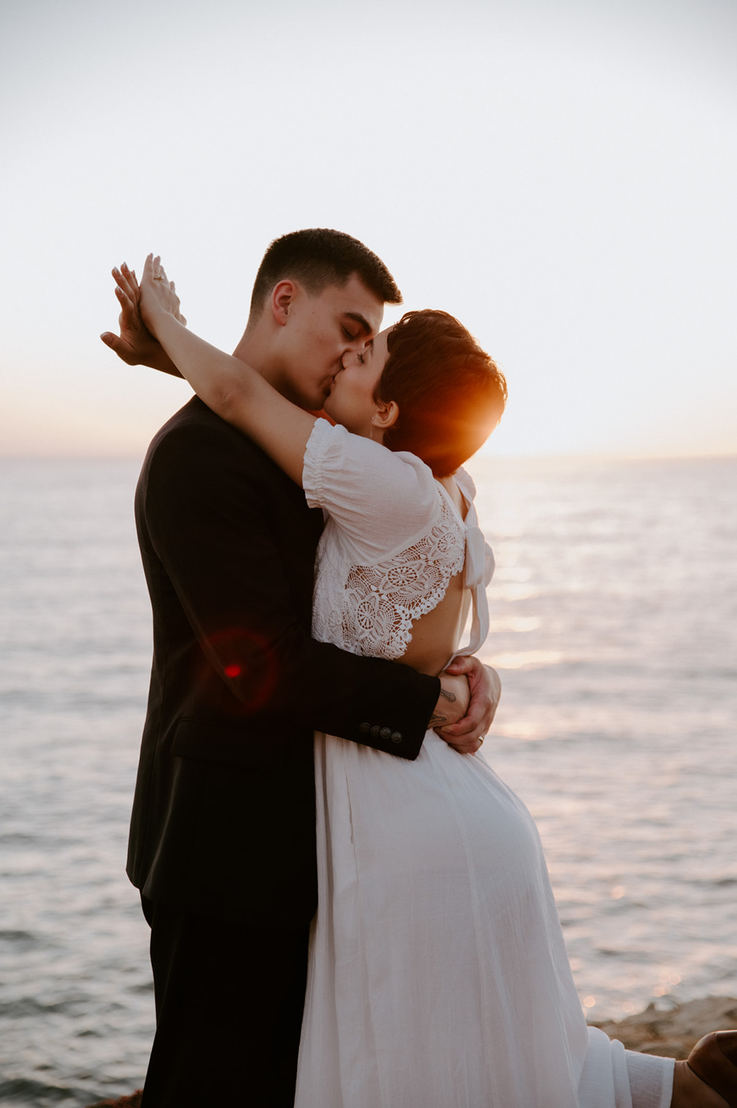 Couple sharing a kiss at sunset on a coastal cliff, golden light wrapping around them during their elopement.
