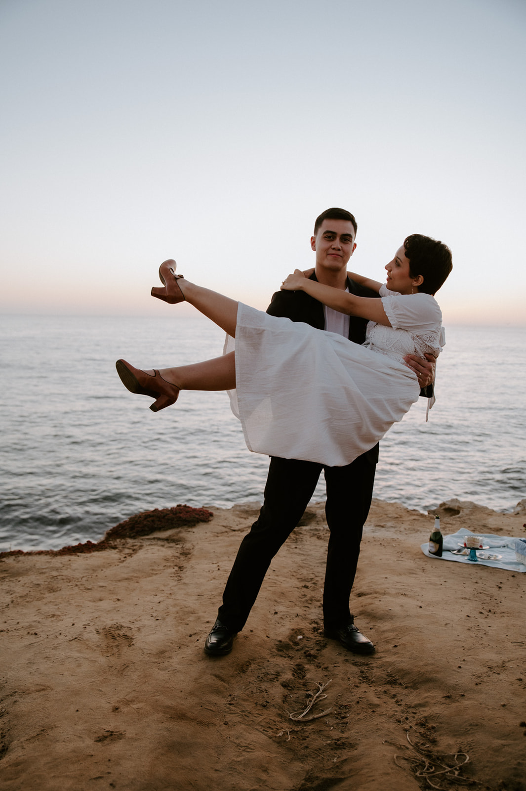 Groom lifting bride in his arms on a seaside cliff, a joyful and spontaneous moment from their elopement checklist.
