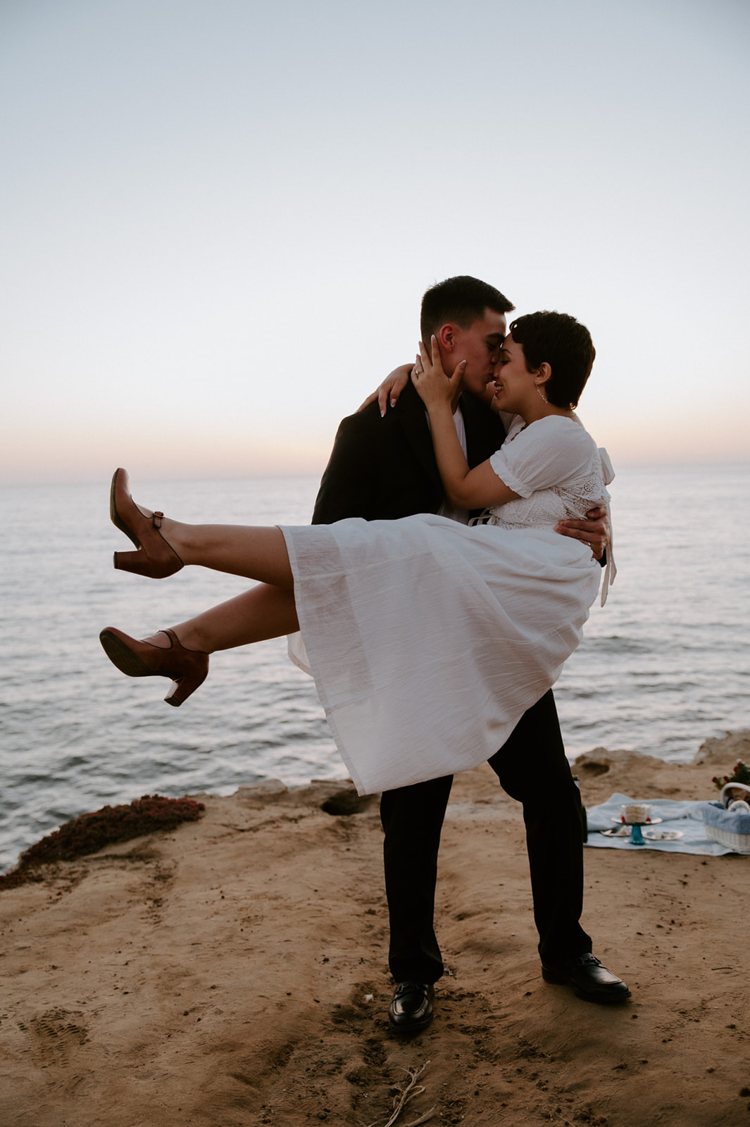 Groom lifting bride off the ground as they kiss on a coastal overlook, a joyful and spontaneous elopement checklist moment.

