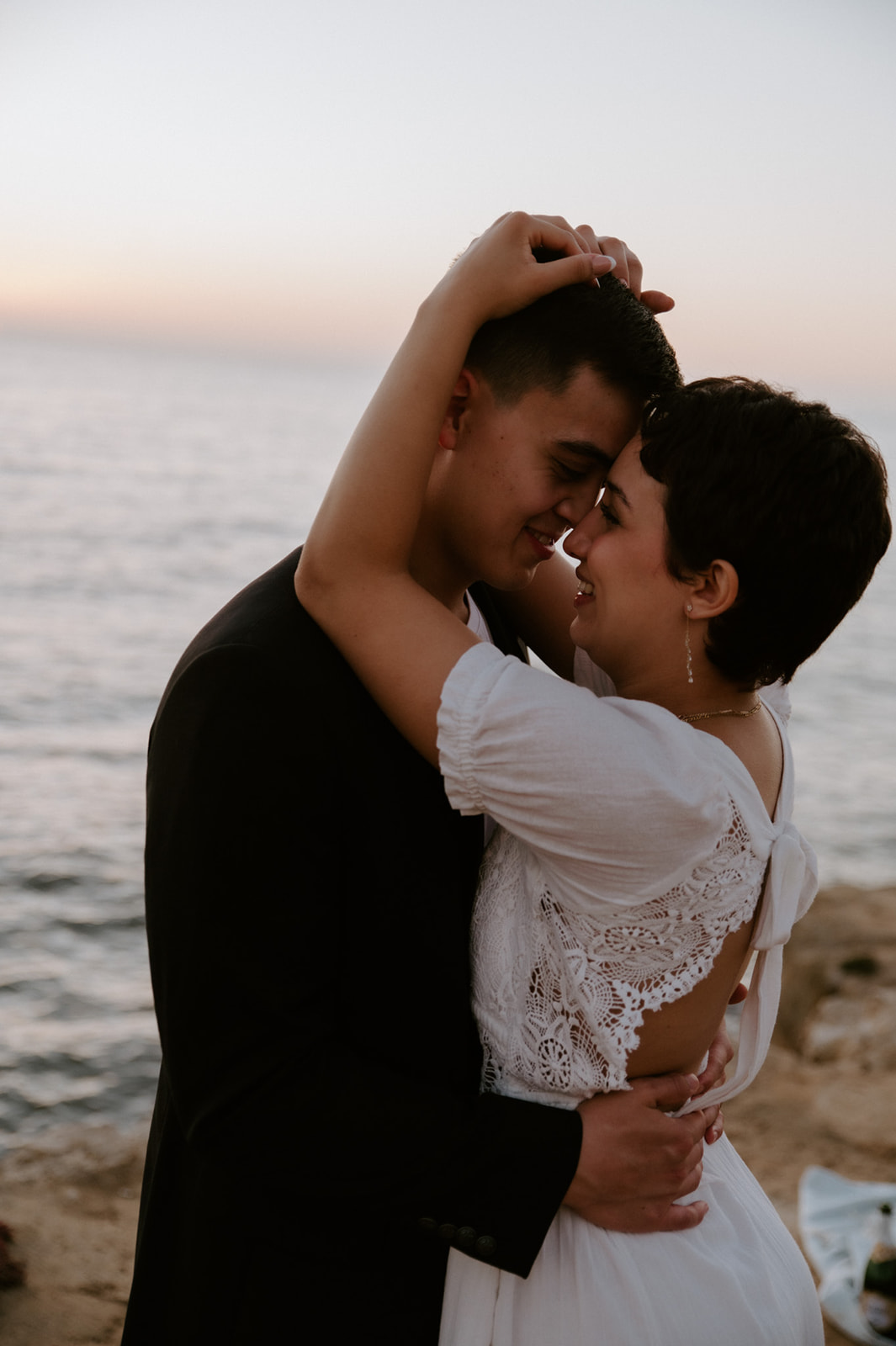 Intimate close-up of a couple smiling forehead to forehead by the ocean, capturing a quiet, emotional elopement moment.
