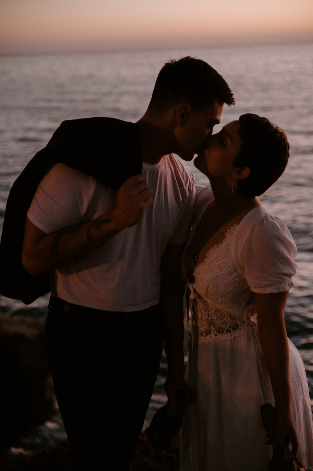 Couple sharing a kiss at golden hour with soft ocean light behind them, capturing the emotion of their elopement.
